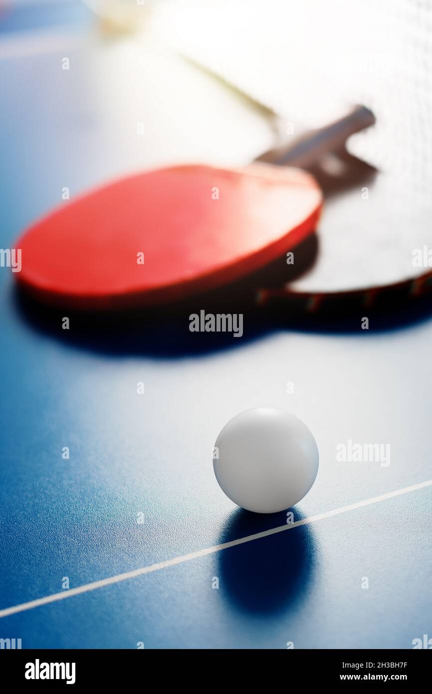 Due racchette da tennis e una palla bianca si trovano su un tavolo da tennis vicino alla rete. Attività ricreative attive e giocare a ping pong. Background sportivo. Foto Stock