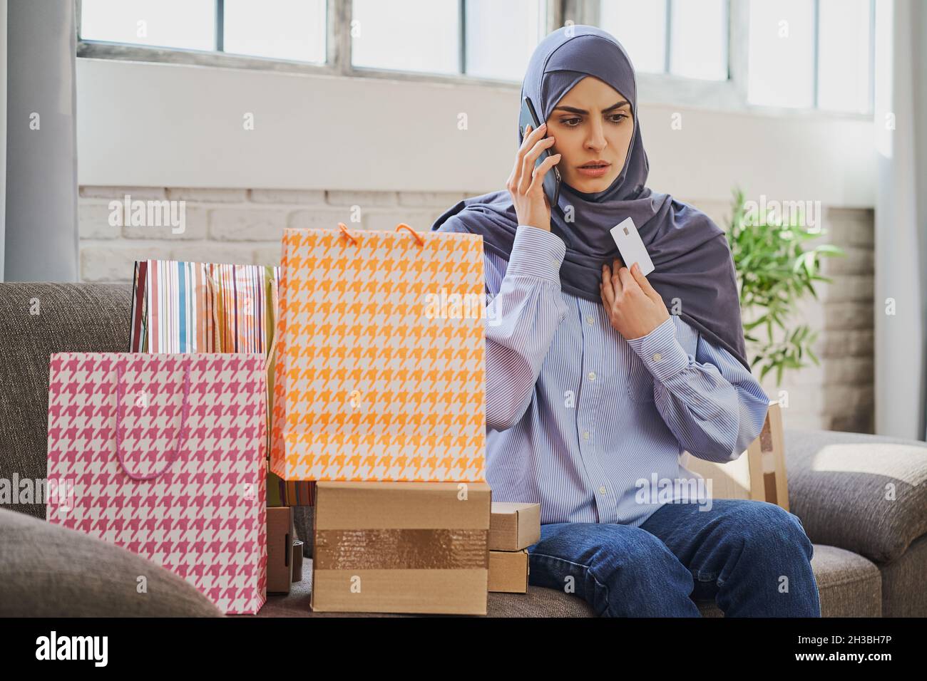 Turbata donna araba che tiene una carta di credito e parla al telefono Foto Stock