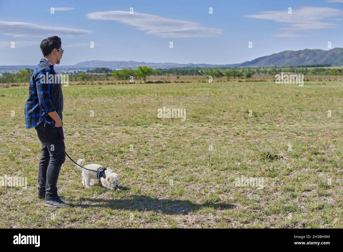 L'uomo latino con il suo puppy pupillle con un'imbracatura in una campagna godendo la passeggiata. Spazio di copia. Orizzontale. Vacanze in Argentina Foto Stock