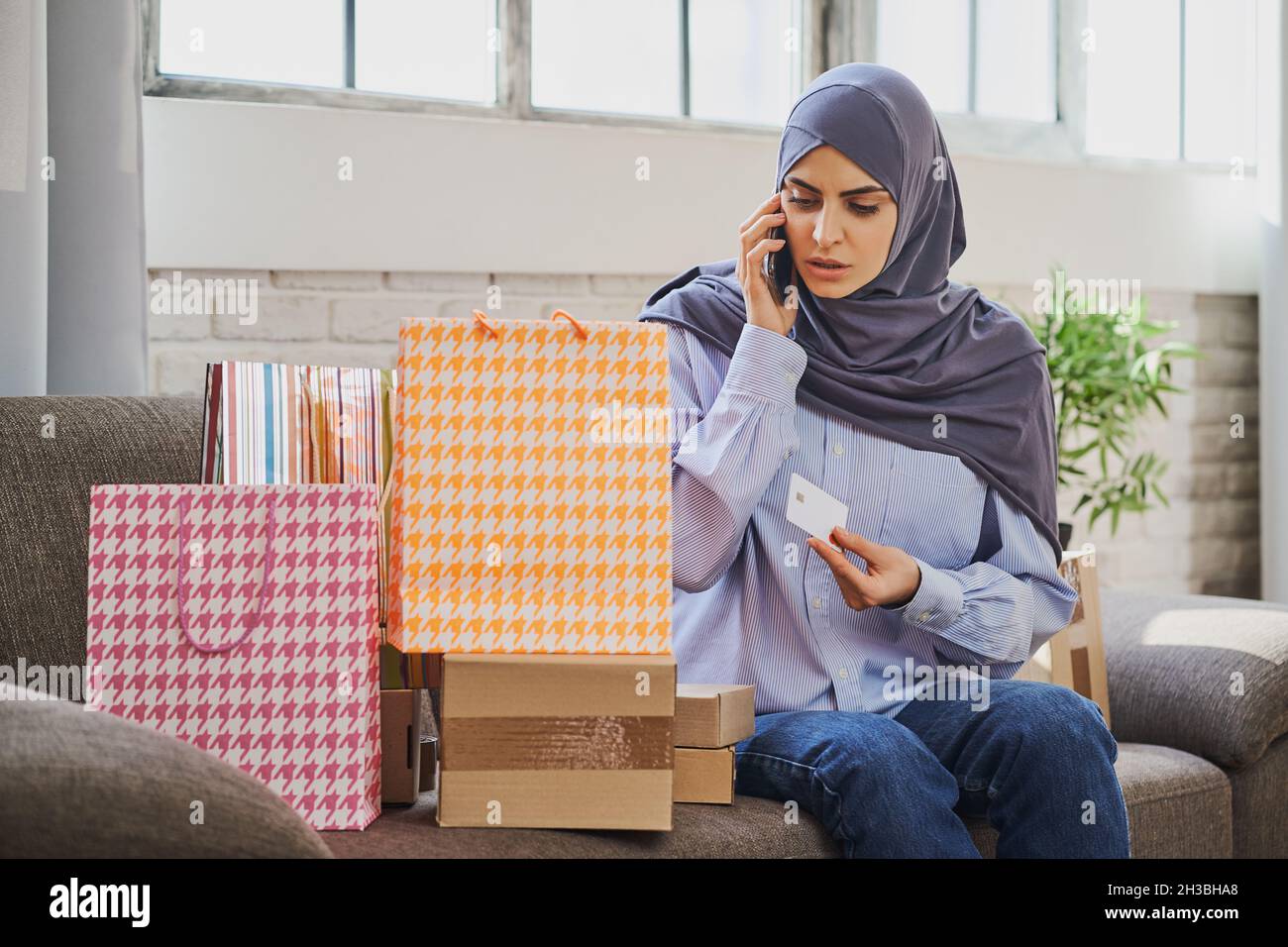 Donna musulmana seria che tiene una carta di credito e parla al telefono Foto Stock
