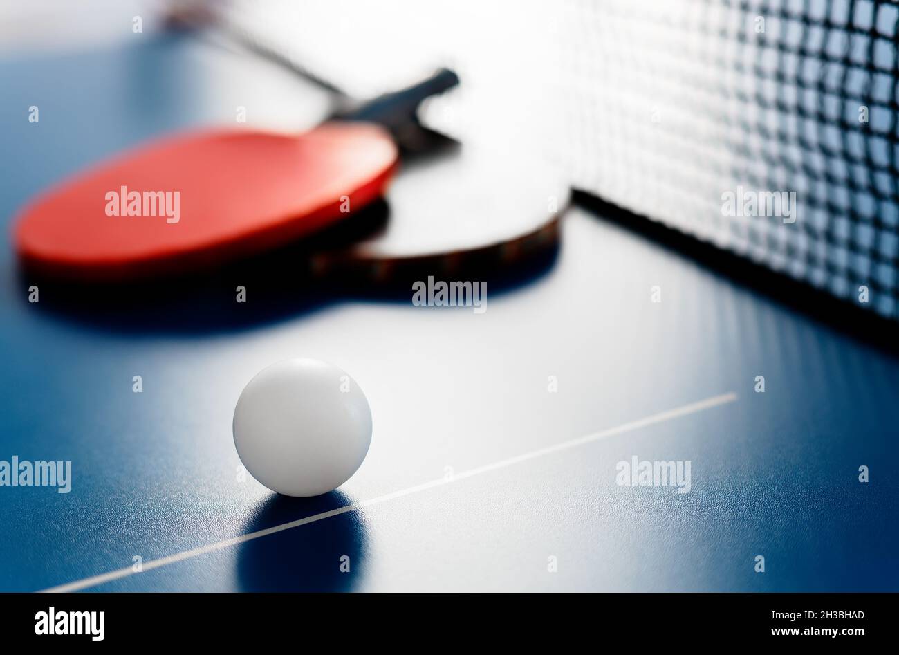 Due racchette da tennis e una palla bianca si trovano su un tavolo da tennis vicino alla rete. Attività ricreative attive e giocare a ping pong. Background sportivo. Foto Stock