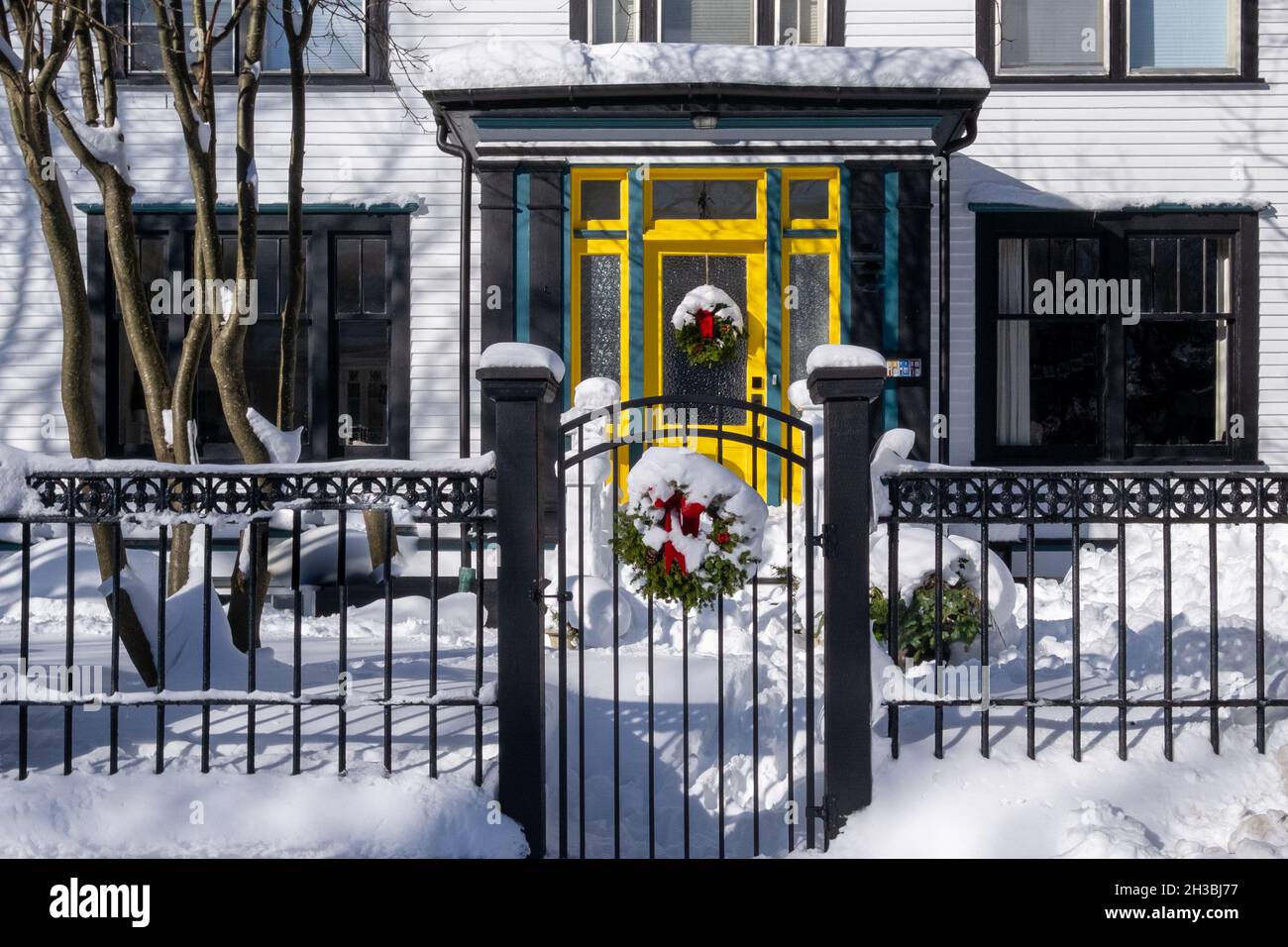 L'ingresso di una casa bianca con una porta di legno giallo e vetro. C'è una recinzione in ferro battuto di metallo nero e cancello nel giardino. Una corona di Natale Foto Stock