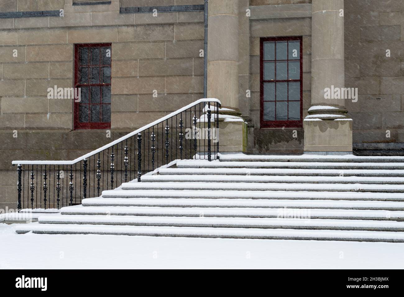 Grandi colonne rotonde in cemento in cima a gradini in marmo con binari in ferro nero per un edificio legale. L'edificio governativo ha una porta rossa alta. Foto Stock
