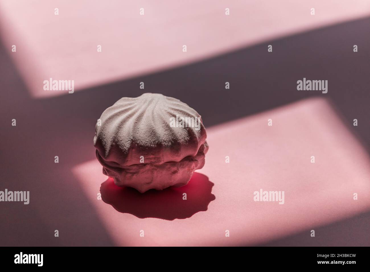 Una marshmallow bianca giace su uno sfondo rosa con ombre. Foto Stock