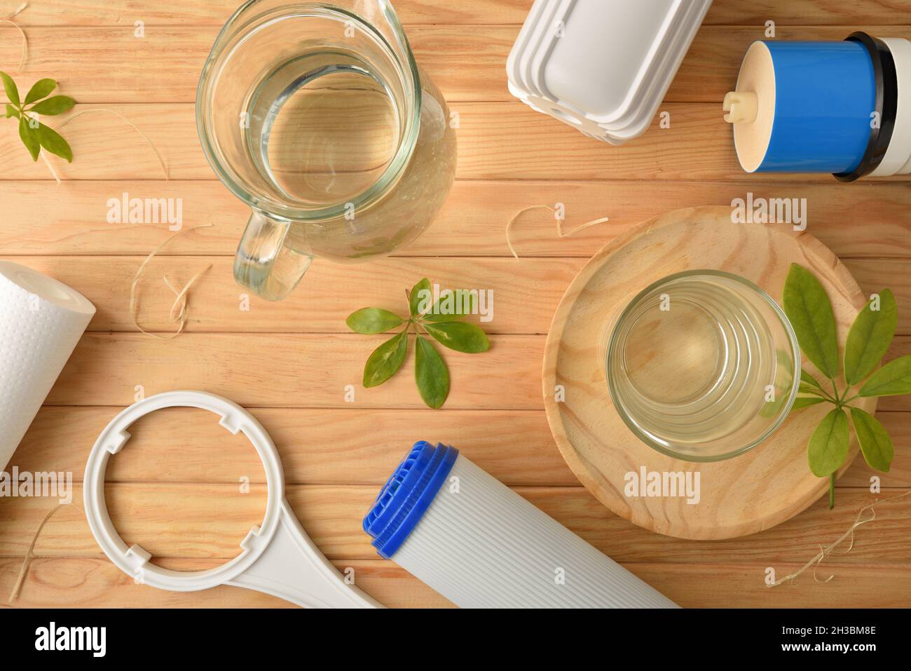 Sistema ad osmosi inversa concetto di purificazione dell'acqua con vetro e caraffa riempito con acqua purificata, filtri e stadi di filtrazione su tavola di legno. Superiore Foto Stock