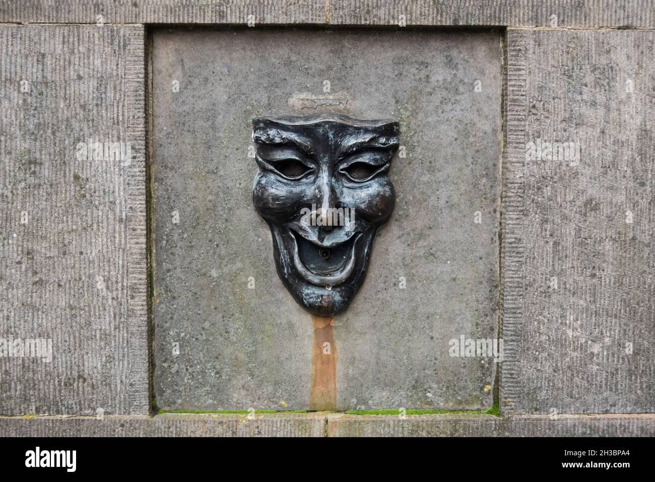 Maschera di bronzo con un volto felice sulla testa del pozzo fuori dall'Edinburgh Fringe Office sul Royal Mile, Edimburgo, Scozia, Regno Unito. Foto Stock