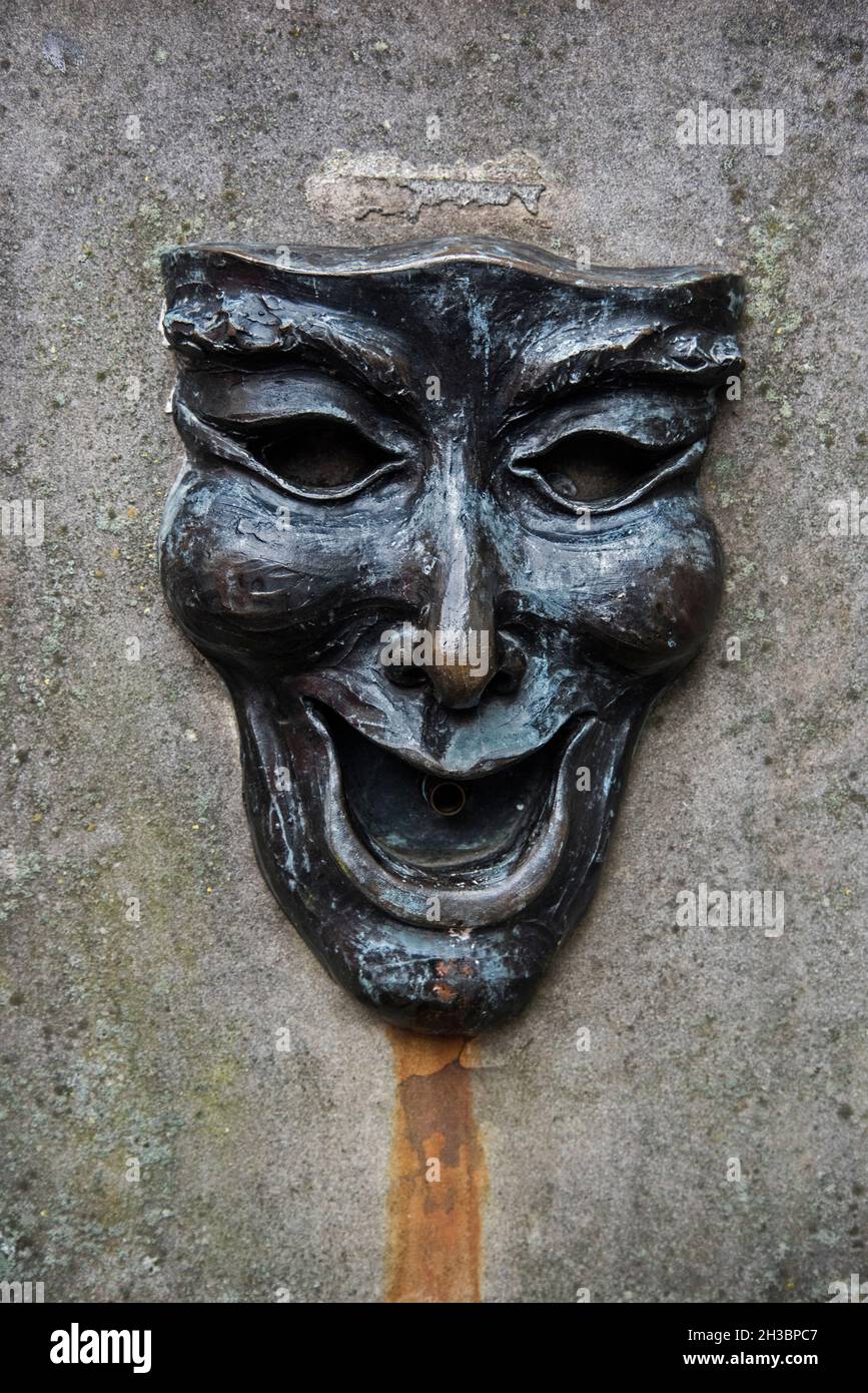 Maschera di bronzo con un volto felice sulla testa del pozzo fuori dall'Edinburgh Fringe Office sul Royal Mile, Edimburgo, Scozia, Regno Unito. Foto Stock
