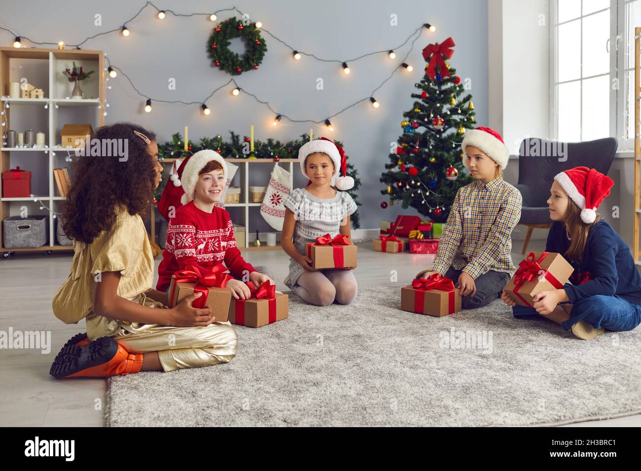 Gruppo di bambini seduti sul pavimento con i loro regali e parlando a casa la mattina di Natale Foto Stock