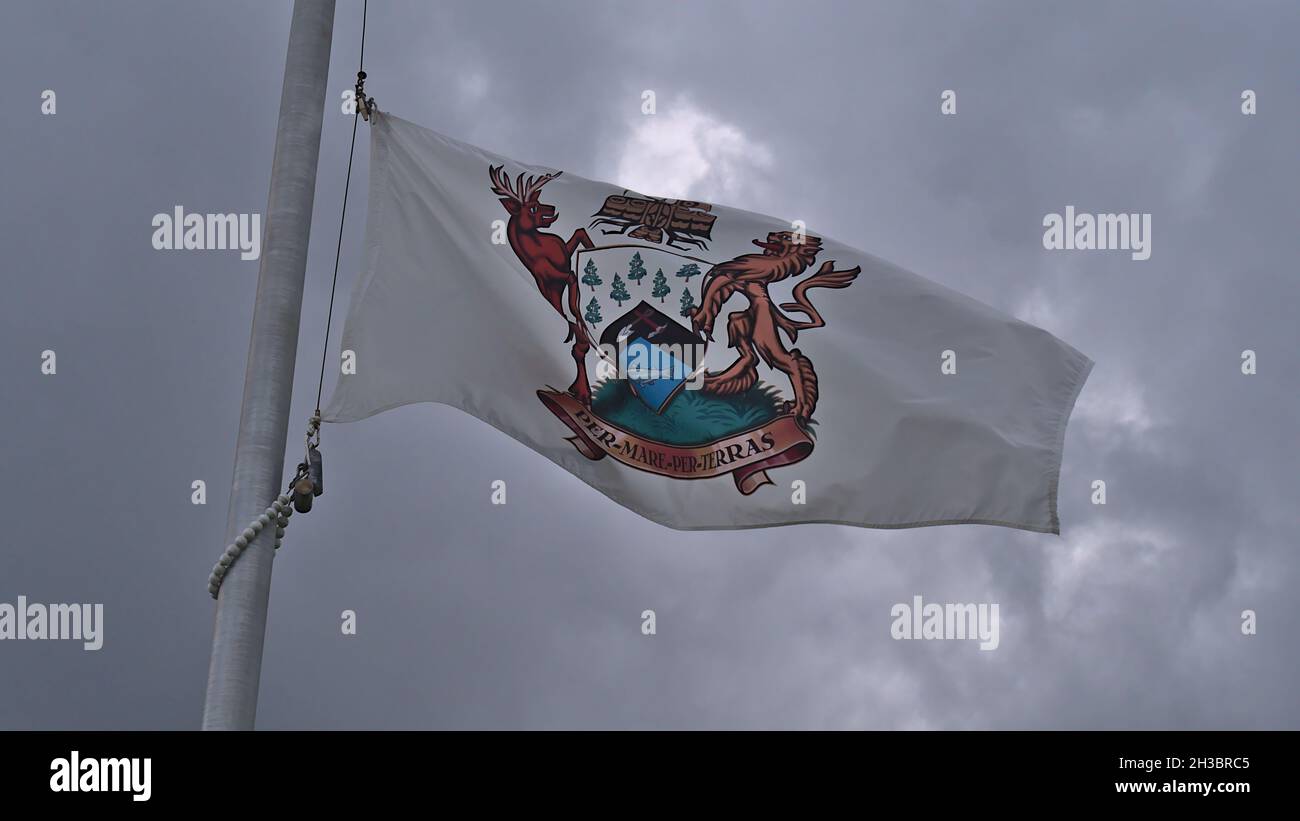 Vista ad angolo basso della bandiera comunale di Port Hardy, Isola di Vancouver con testo latino "per mare per terras" il giorno nuvoloso nella stagione autunnale. Foto Stock