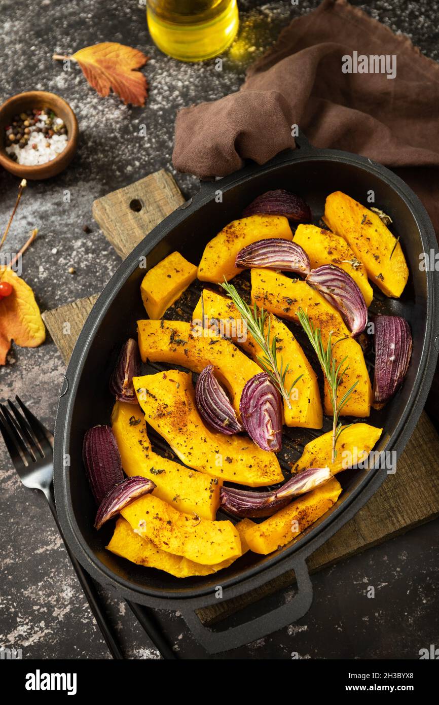 Affettare le zucche con rosmarino e cipolla viola, cuocere cibi freschi e sani con spezie su sfondo di pietra scura. Cheto o paleo dieta vegetariano vegano o vegano Foto Stock