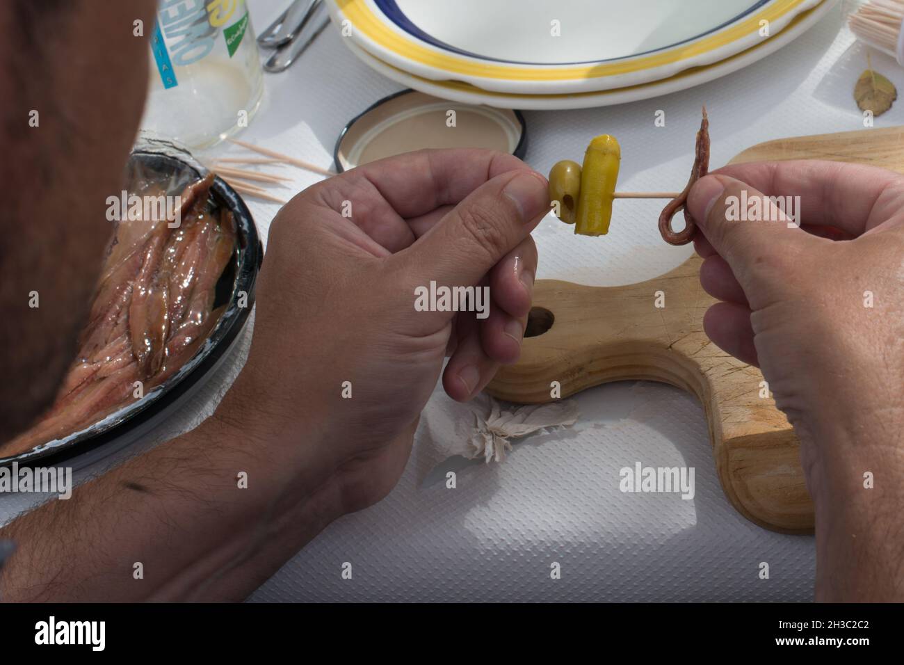 Uomo irriconoscibile che prepara tapas spagnole con peperoncino, olive e acciughe su uno spiedino di legno. Mani Foto Stock