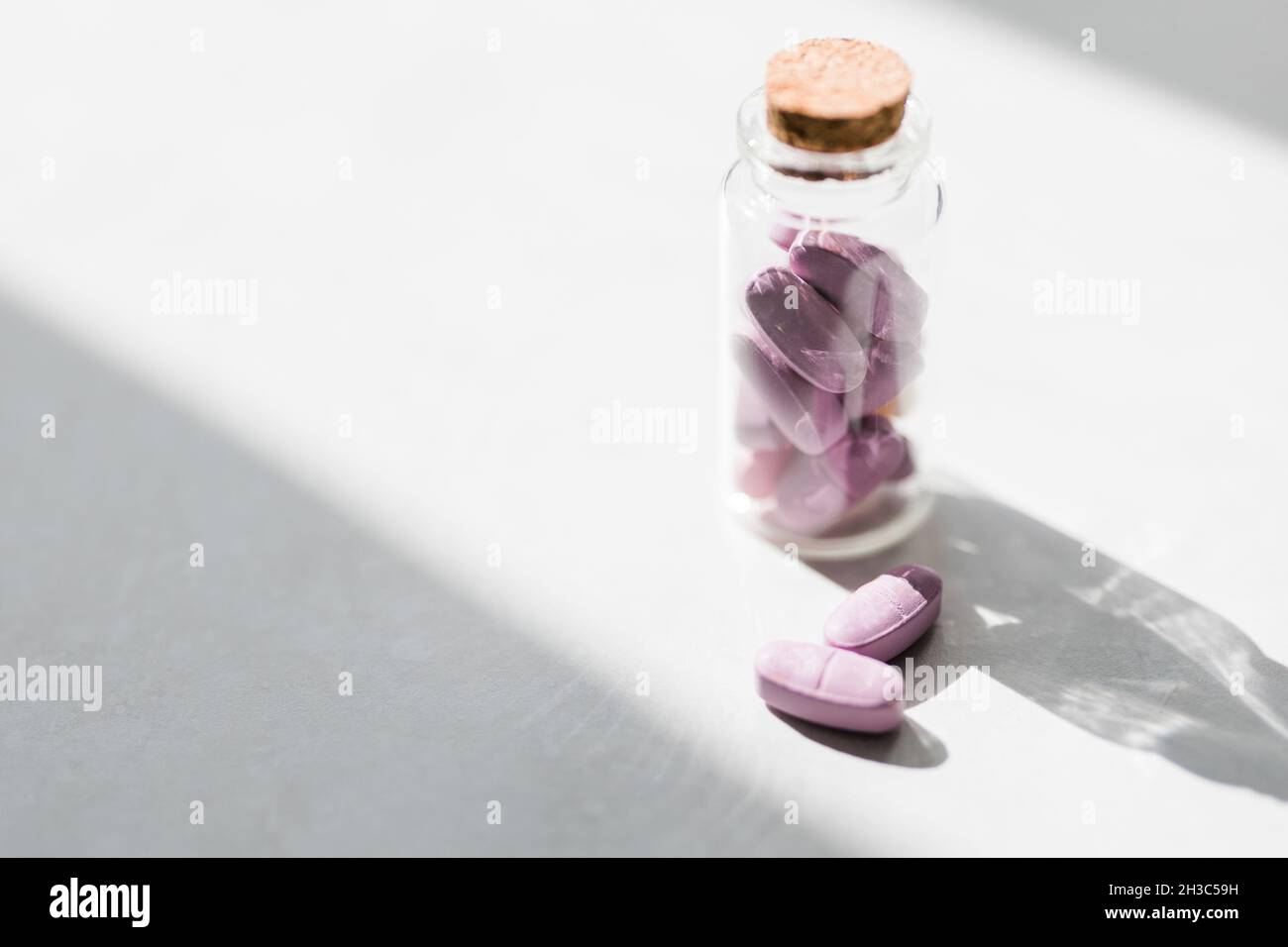pillole vitaminiche rosa in un vaso di vetro jn tavola bianca. Medicina conservativa. Concetto di assistenza sanitaria. Foto Stock