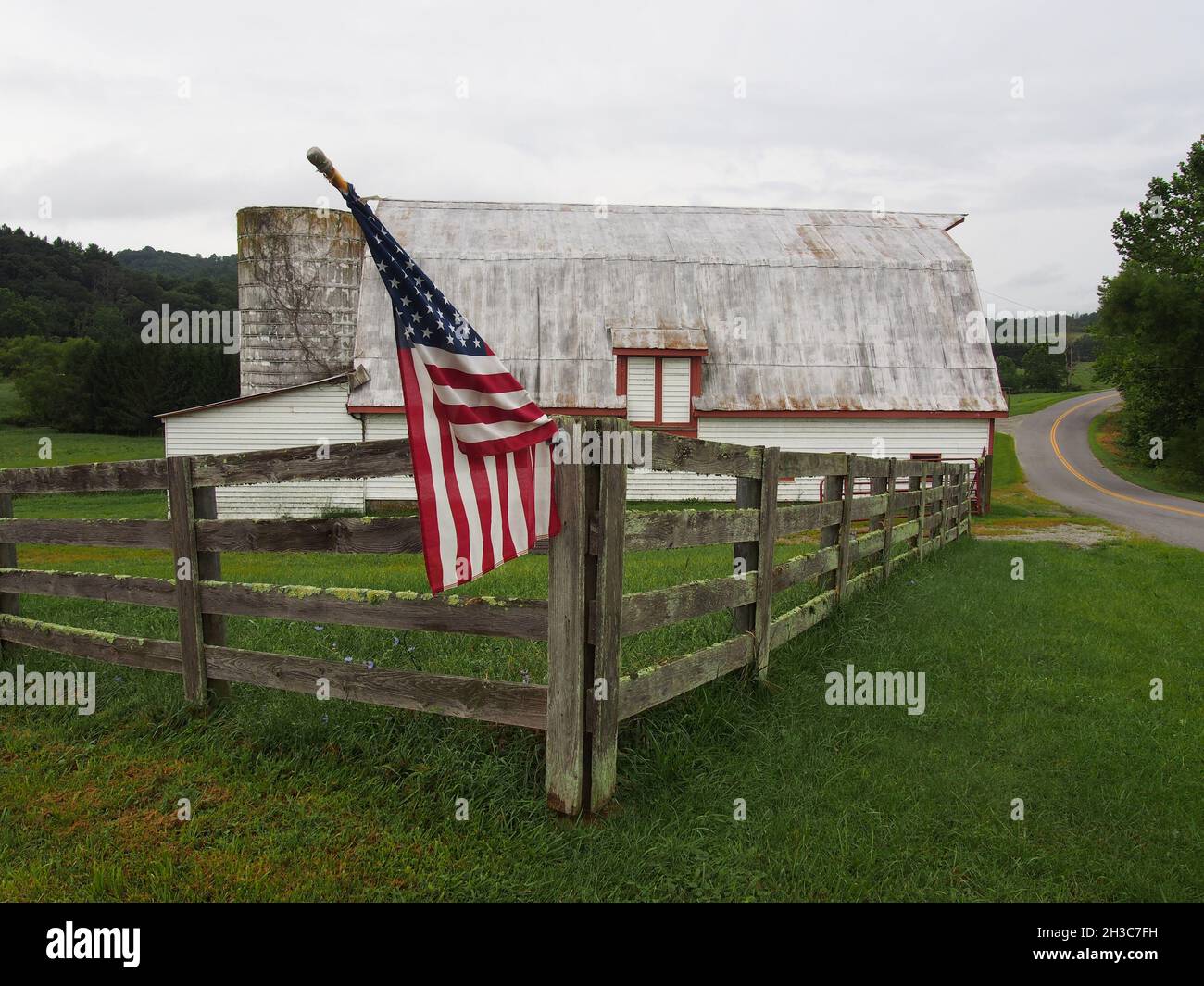 Una bandiera americana vola su una recinzione post-e-rail in un vecchio fienile in Virginia, USA, 2021 © Katharine Andriotis Foto Stock