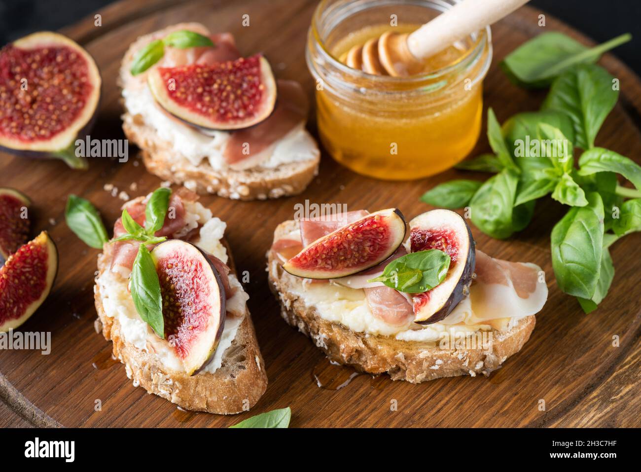 Fig e prosciutto bruschetta servito con basilico e miele su un asse di legno, vista a primo piano. Antipasto italiano Foto Stock