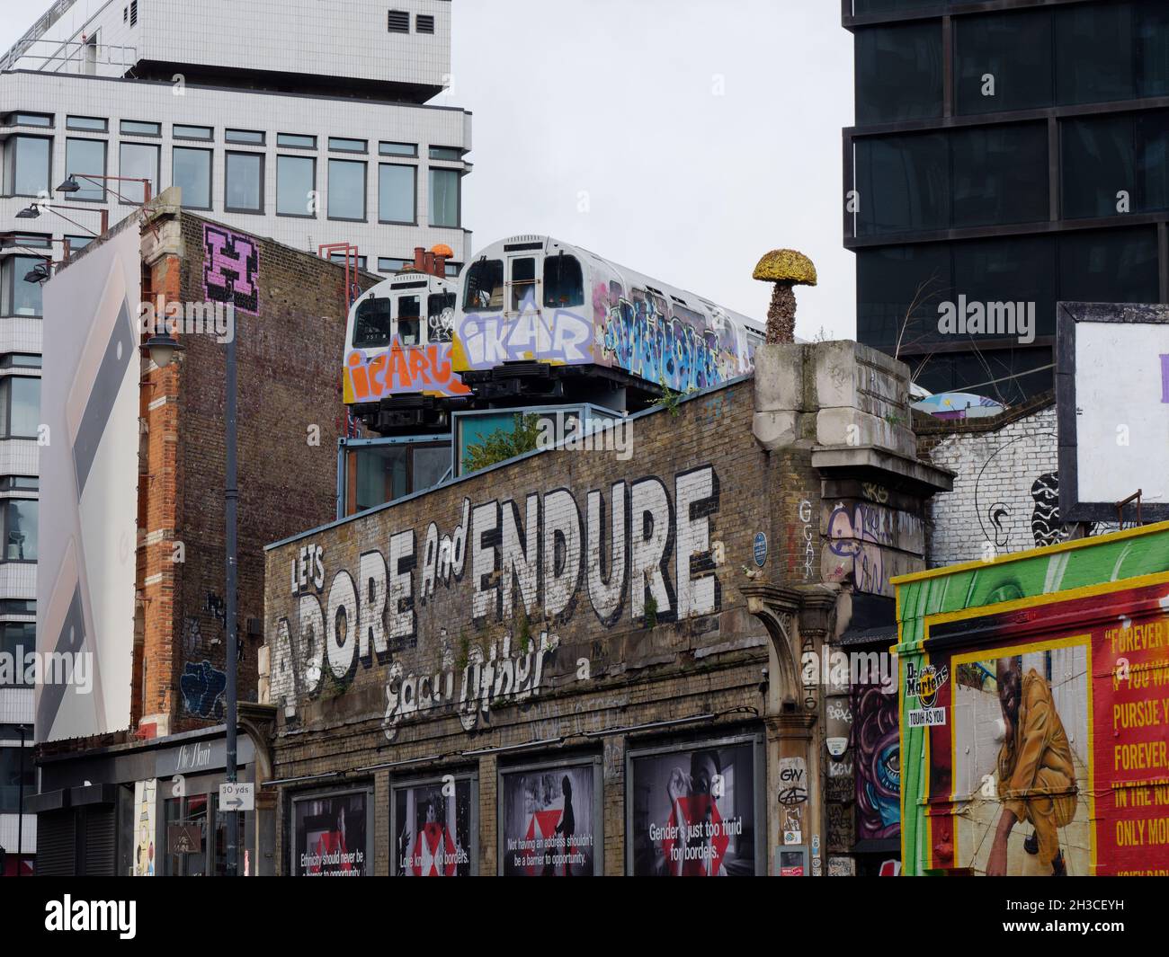 Great Eastern Street a Shoreditch con i famosi Lets adorare e sopportare l'altro segno e treni della metropolitana sopra un edificio. Londra Foto Stock