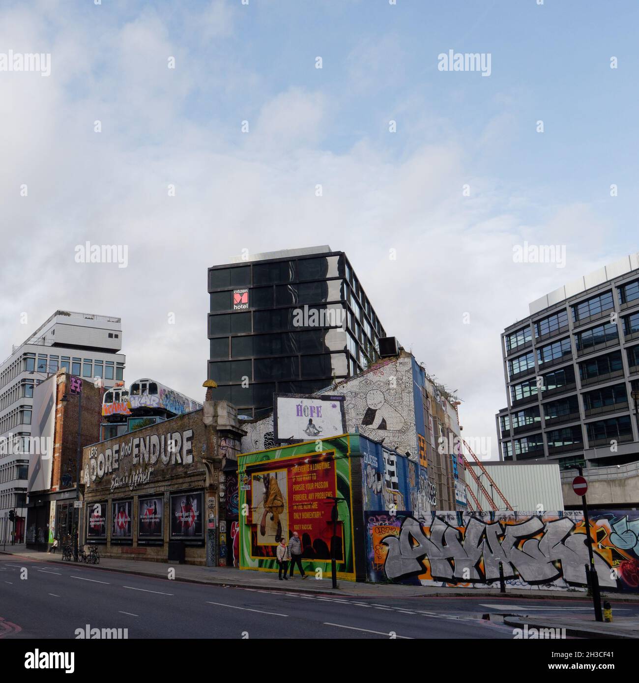 Great Eastern Street a Shoreditch con i famosi Lets adorare e sopportare l'altro segno e treni della metropolitana sopra un edificio. Londra Foto Stock