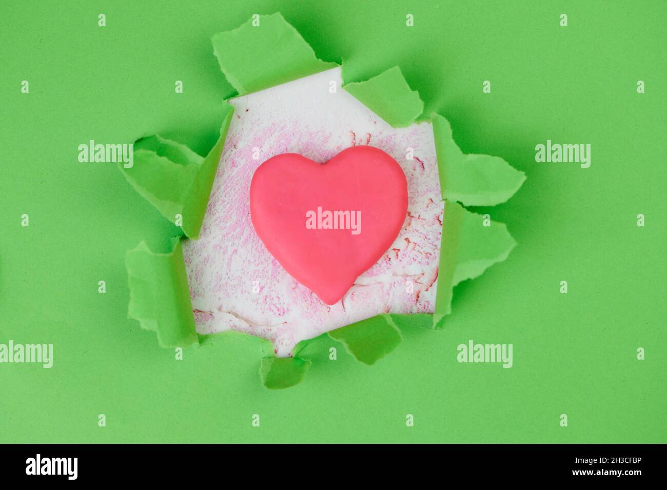 carta verde strappata con un cuore rosa al centro Foto Stock