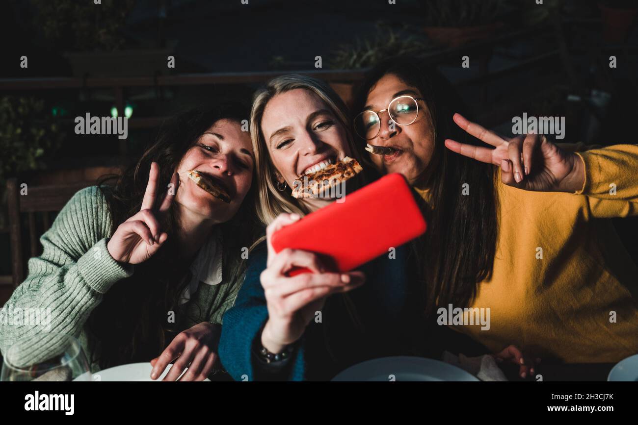 Amici multirazziale divertirsi a fare selfie con telefono cellulare al ristorante pizzeria bar all'aperto - fuoco morbido sul viso centrale ragazza Foto Stock