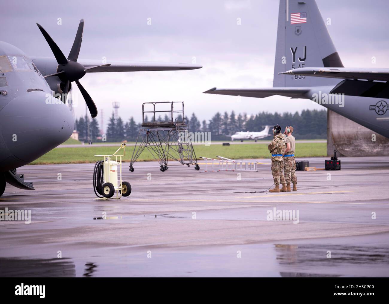 Due manutentori con il 374° Maintenance Group osservano il funzionamento del motore C-130J Super Hercules mentre un C-12J Huron atterra sulla linea di volo alla base aerea di Yokota, Giappone, 9 settembre 2021. Il 374th MXG mantiene gli aerei C-130J, C-12J e UH-1N che supportano l'airlift intra-teatro e il trasporto di visitatori distinto per le forze aeree del Pacifico. (STATI UNITI Air Force foto di Tech. SGT. Amanda Sampson) Foto Stock