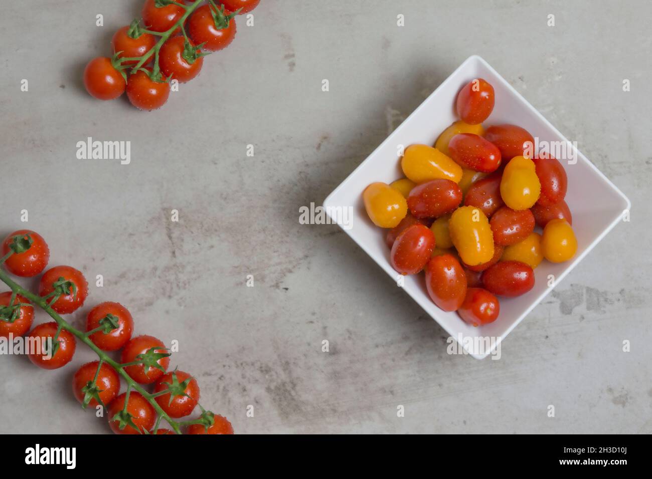 pomodori piccoli rossi e gialli in ciotola quadrata bianca. rami di pomodori rossi sono nelle vicinanze. Disposizione piatta Foto Stock