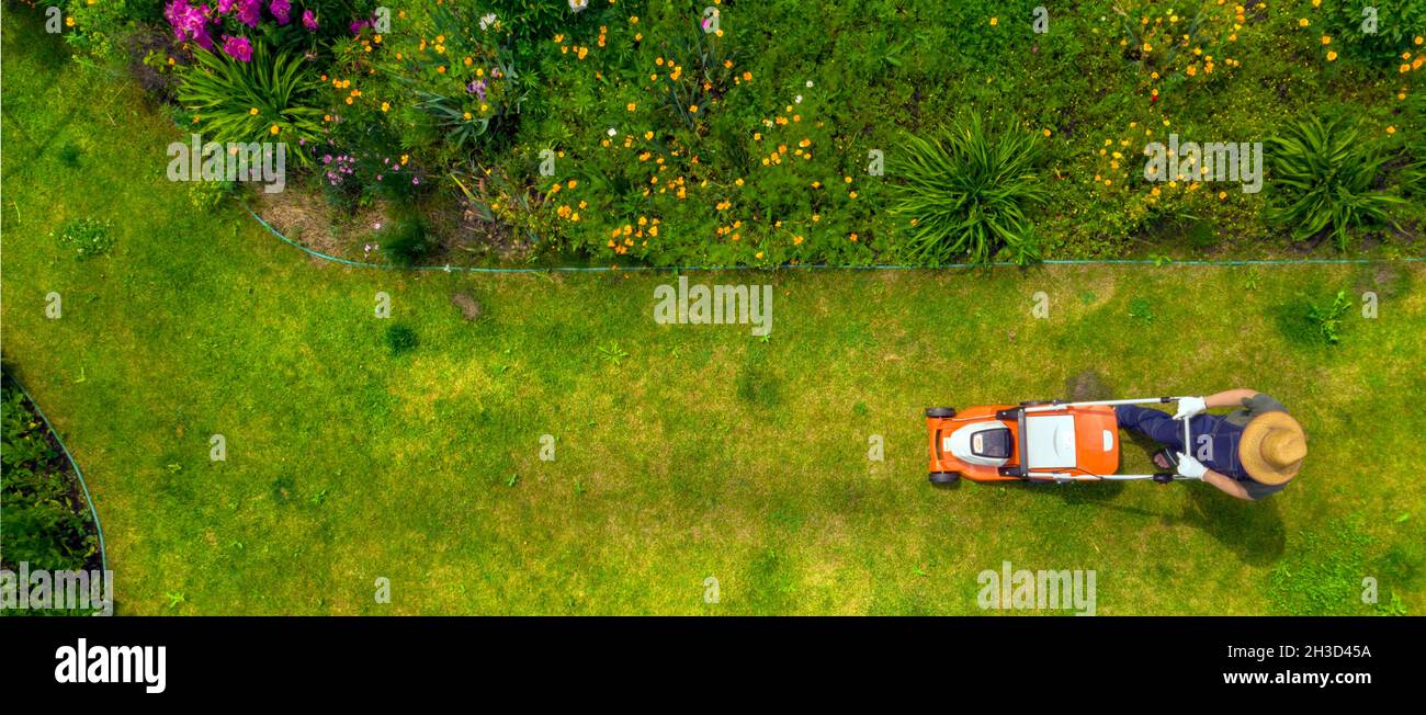 Un giovane uomo sta falciando un prato con un tosaerba. Foto Stock