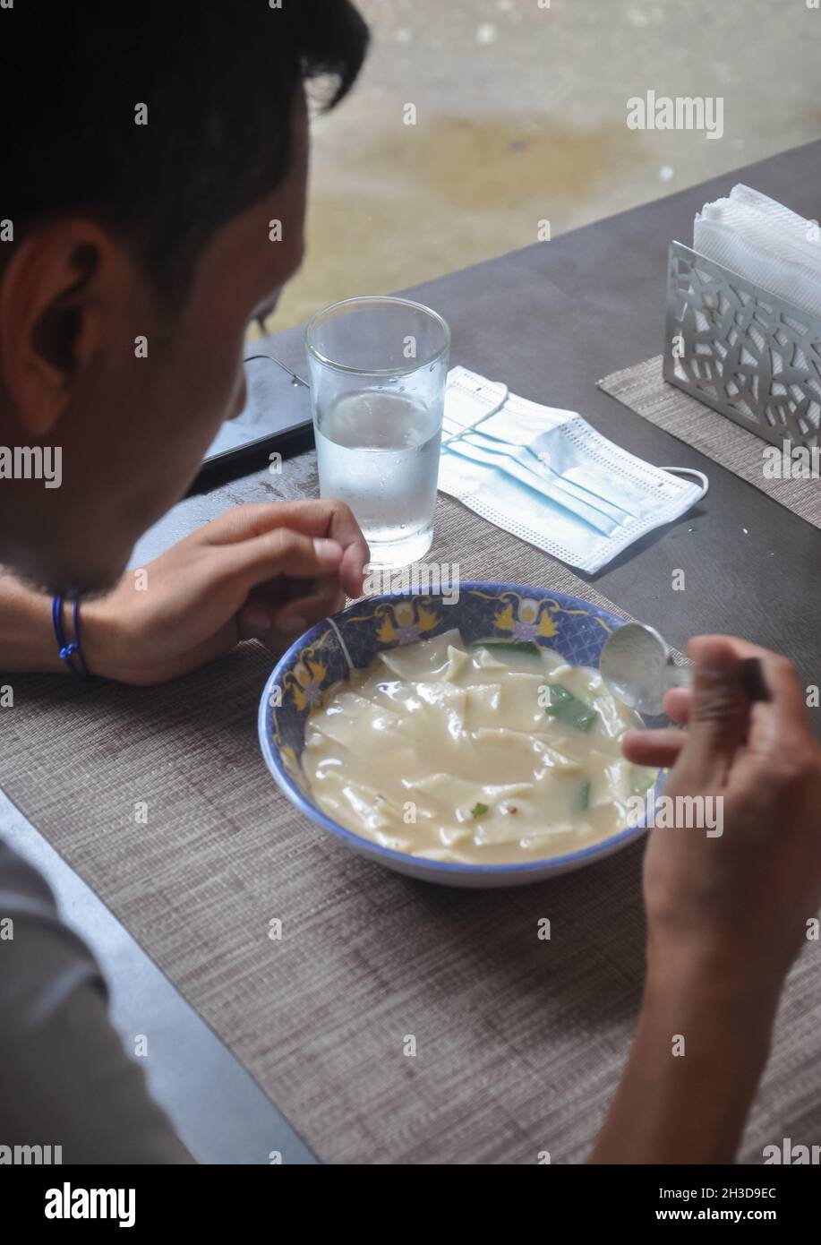 Un giovane asiatico che mangia thenthuk (cugino tibetano) in un caffè tibetano Foto Stock