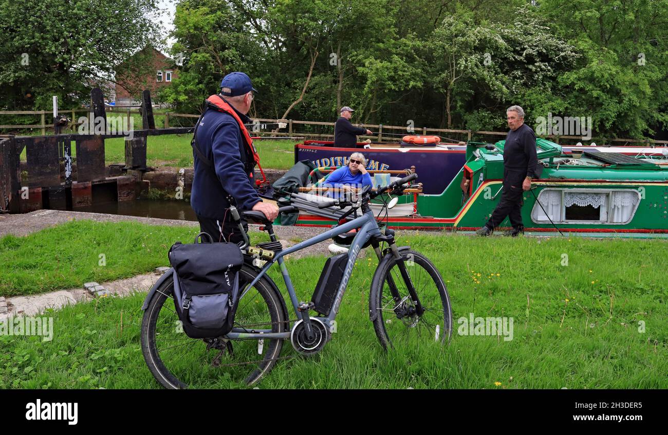 Un equipaggio di barca stretto chiacchiera con un portiere volontario mentre lavorano giù il volo di Wigan, il volontario sta usando una bici per viaggiare tra le serrature. Foto Stock