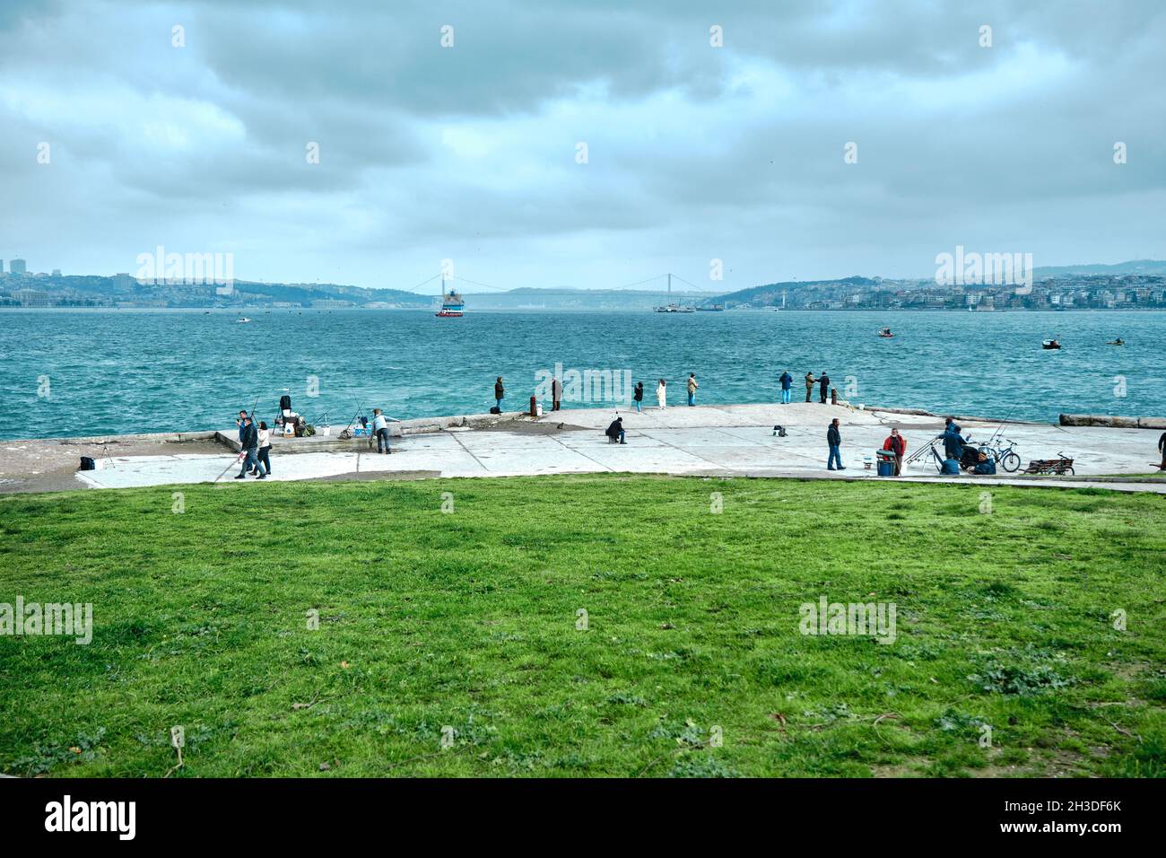 Una nave enorme nel ponte di bosforo istanbul vicino al distretto di sarayburnu con molte persone a piedi e la pesca in riva al mare durante il tempo coperto Foto Stock