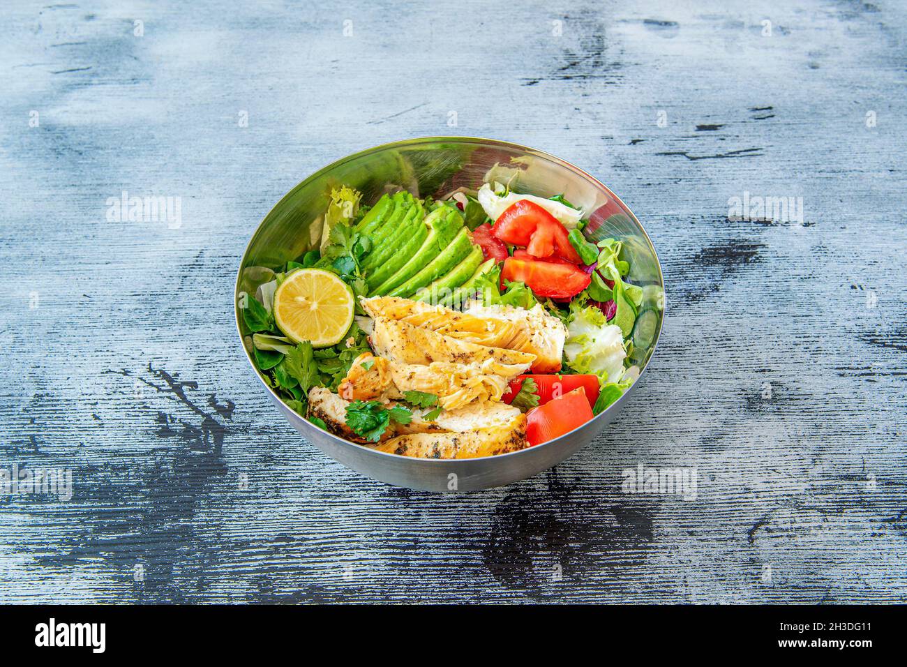 Ciotola di avocado maturo con pollo fritto e insalata di pomodoro e lattuga con coriandolo e limone Foto Stock