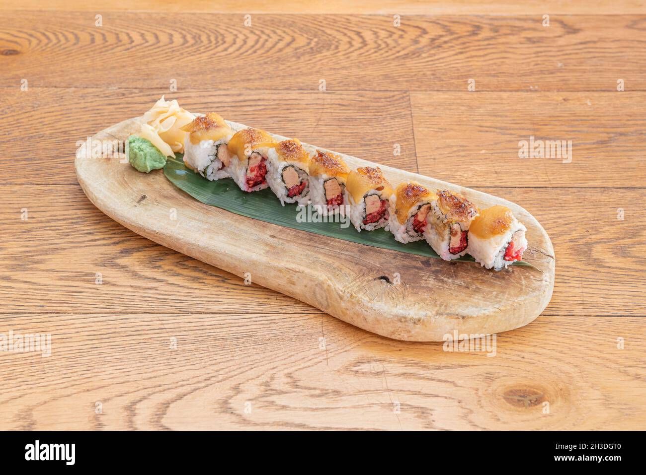 Rotolo di uramaki di sushi di foie e lamponi con riso giapponese, salmone flambé, wasabi e ginseng su foglia di banana Foto Stock