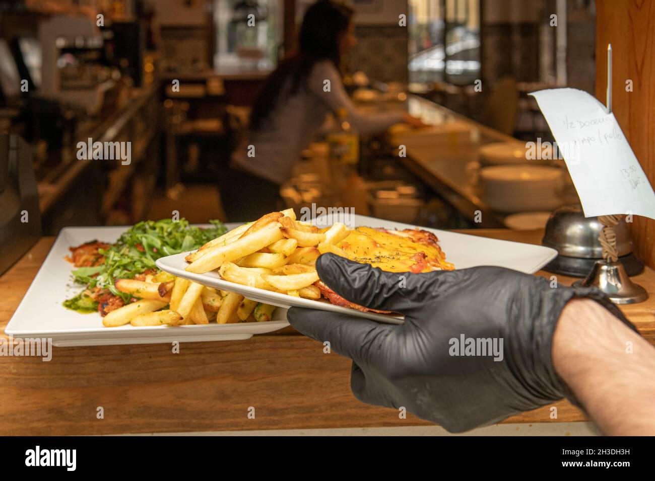 La mano dello chef consegna un ordine con vitello e formaggio milanese al banco di un ristorante Foto Stock