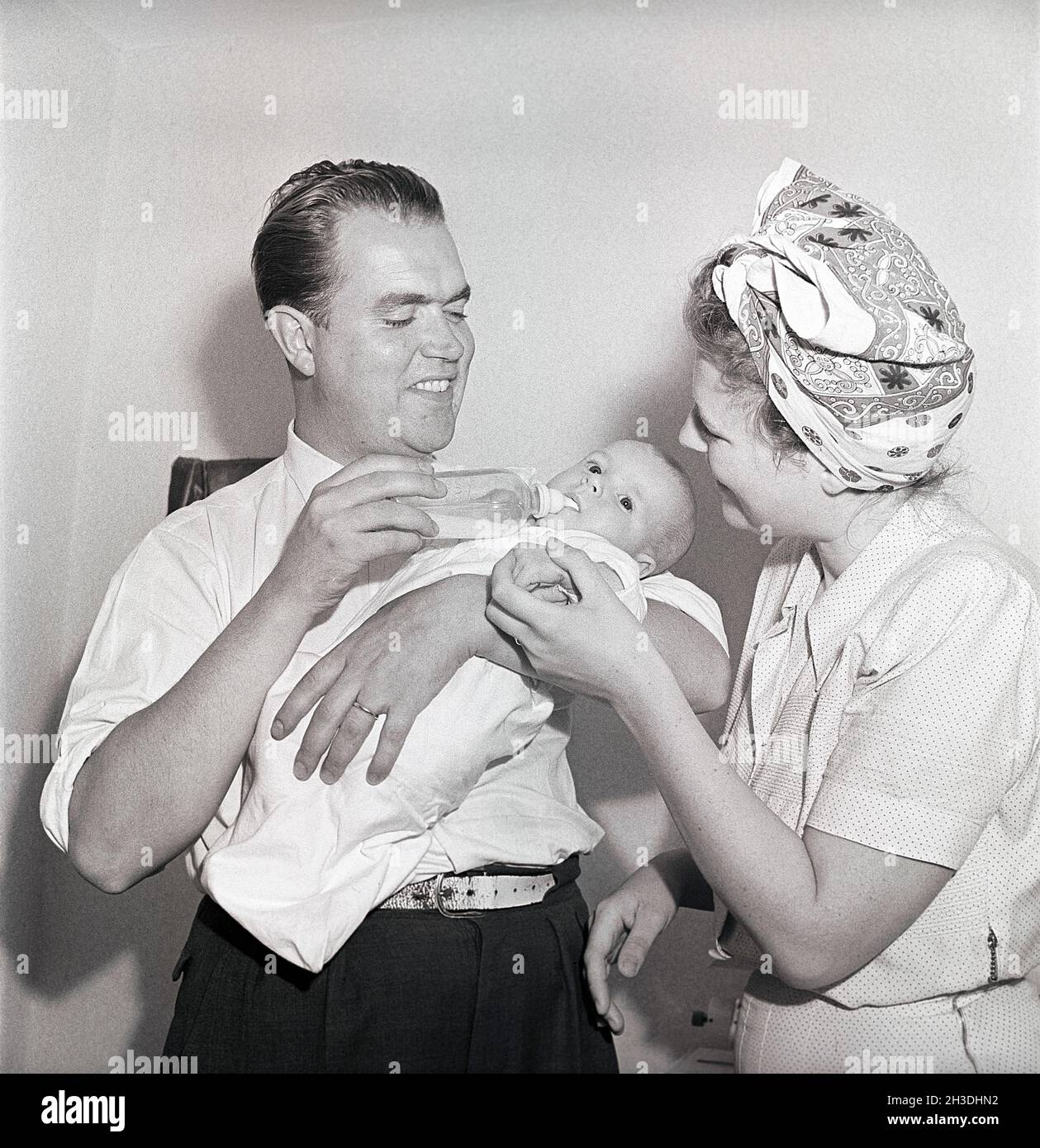 Genitori negli anni '40. Un bambino appena nato sta bevendo da un biberon. Il padre lo tiene e la madre guarda, sorridendo. Svezia 1947. Rif. Kristoffersson AD13-11 Foto Stock