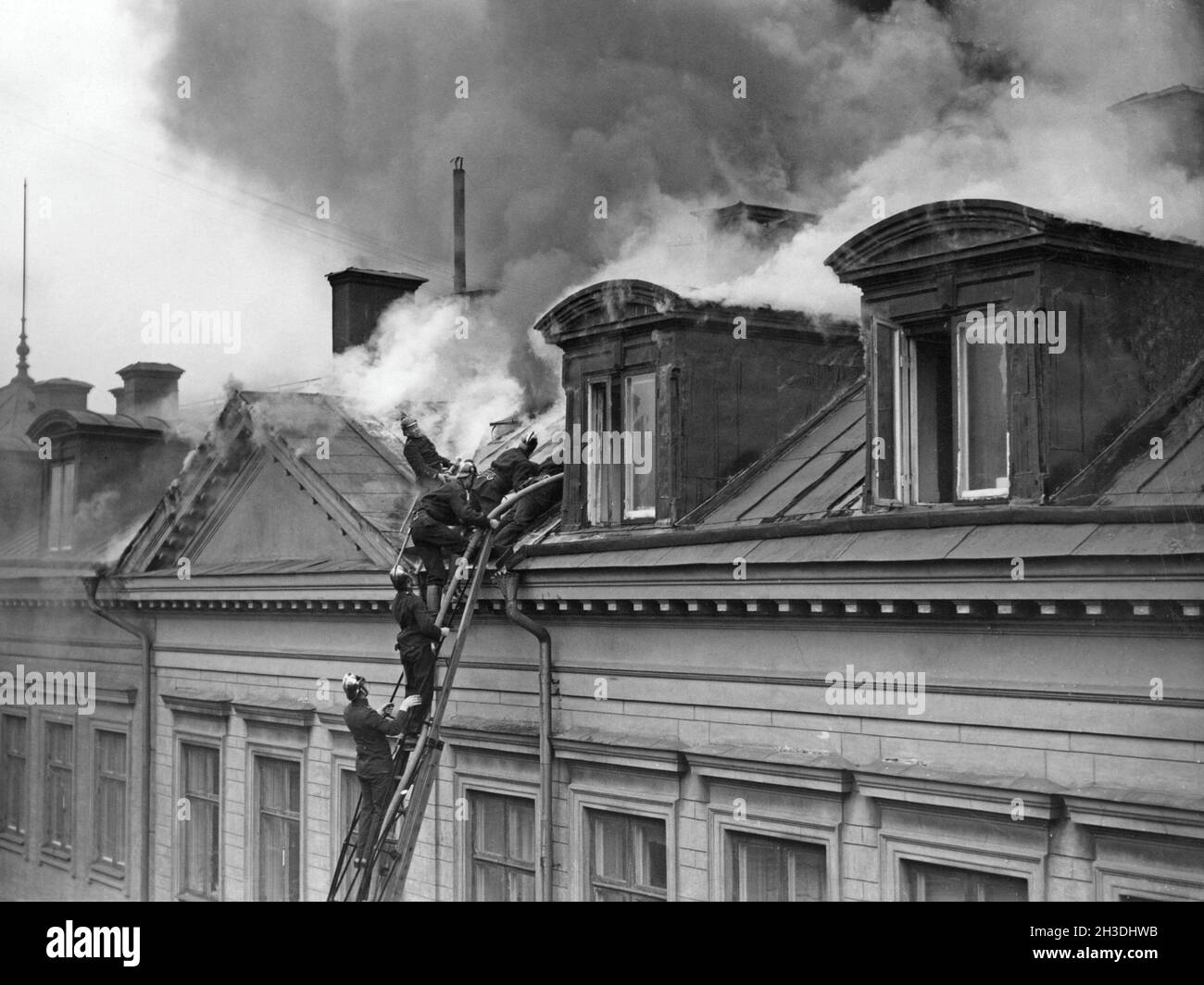 Fuoco negli anni '20. Vigili del fuoco su una scala per raggiungere l'ultimo piano e soffitta di un edificio in fiamme a Malmskarnadsgatan a Stoccolma negli anni '20. Un tubo è visibile sulla scala e il vigile del fuoco cerca di spegnere il fuoco. Foto Stock