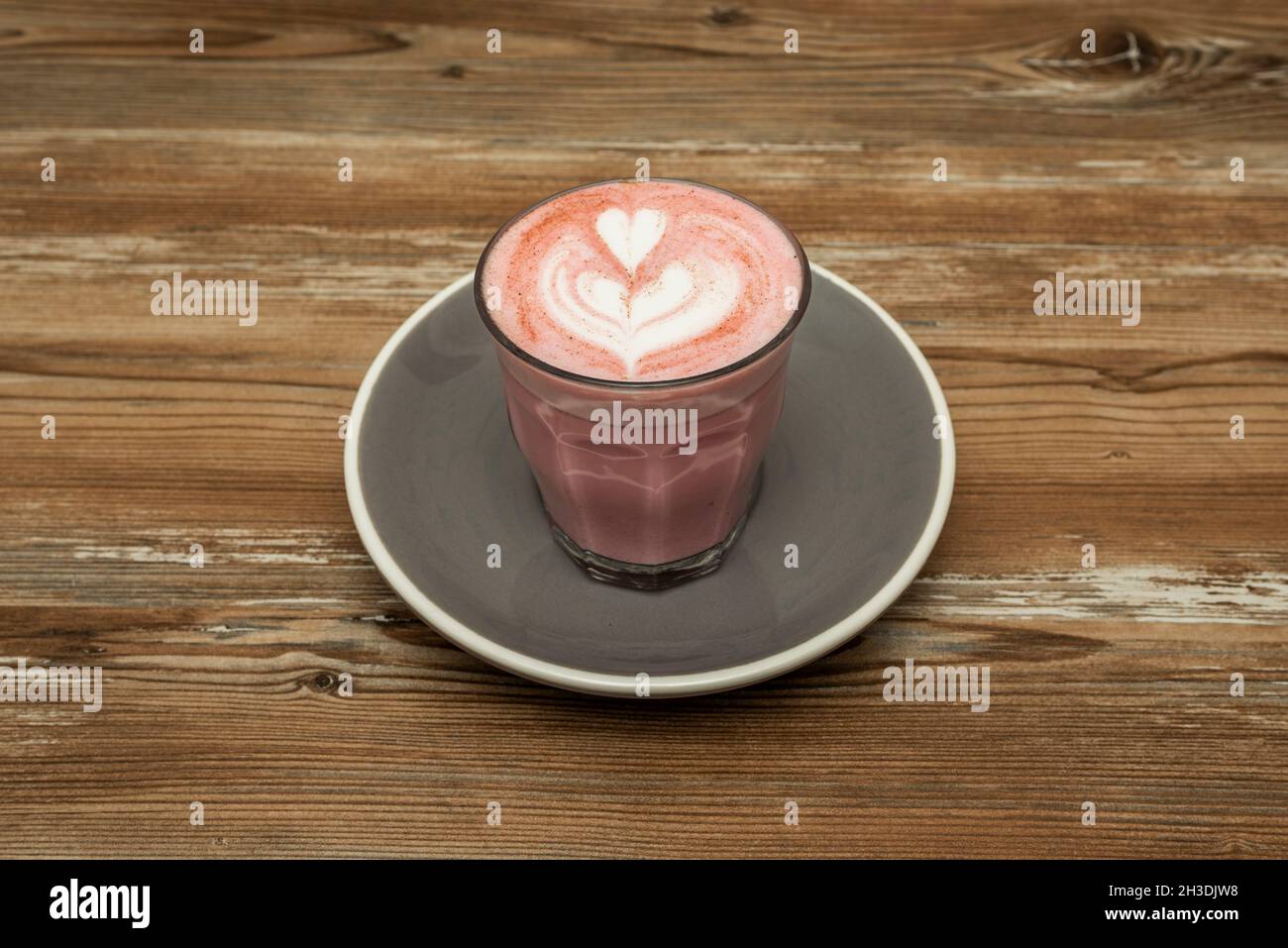 Latte rosa servito da un barista che attira i cuori su un tavolo di legno Foto Stock