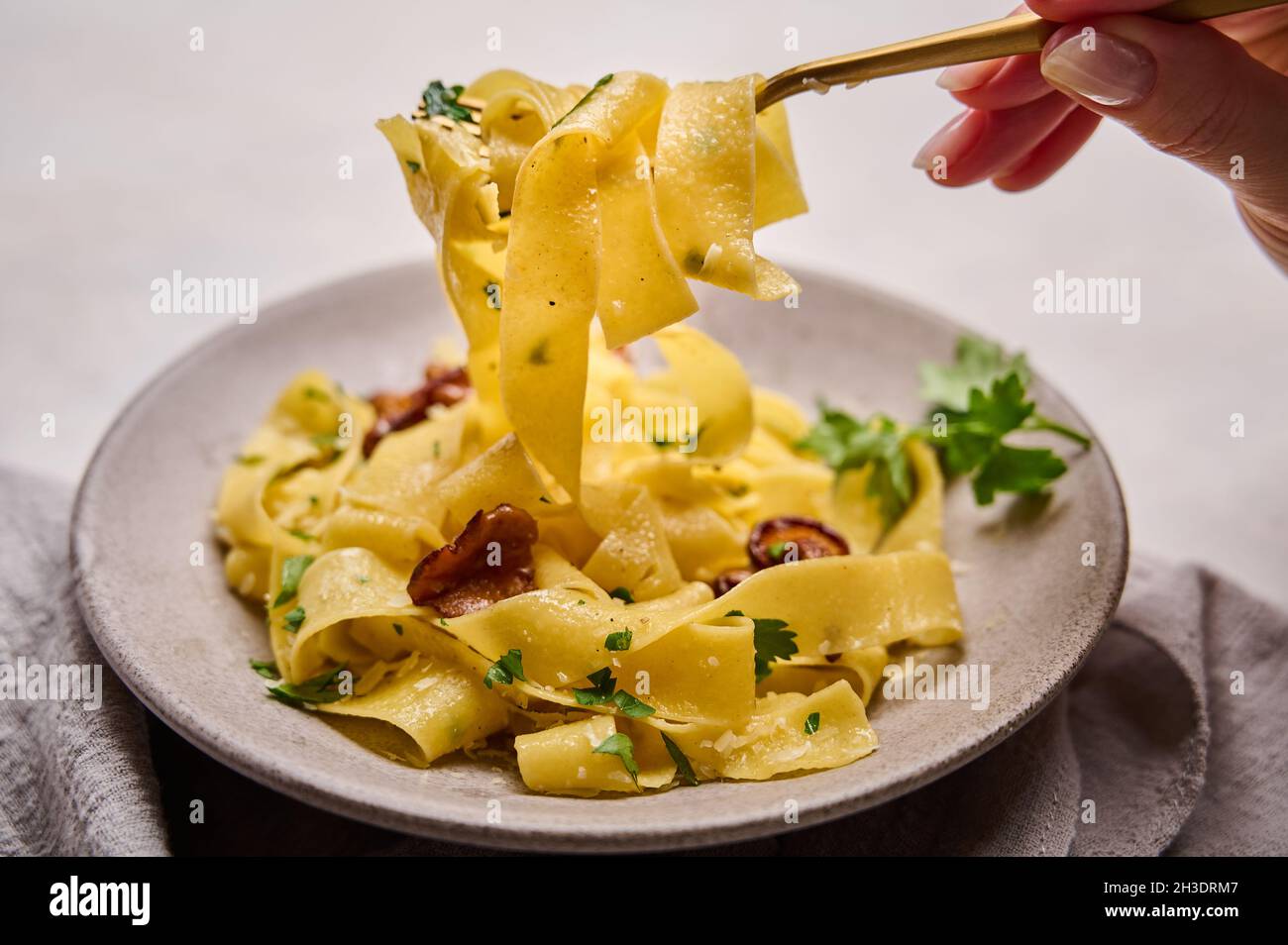 La mano della donna tiene una forchetta con pappardelle di pasta italiana  con funghi, cravatte, formaggio e prezzemolo. Macro, messa a fuoco  selettiva Foto stock - Alamy