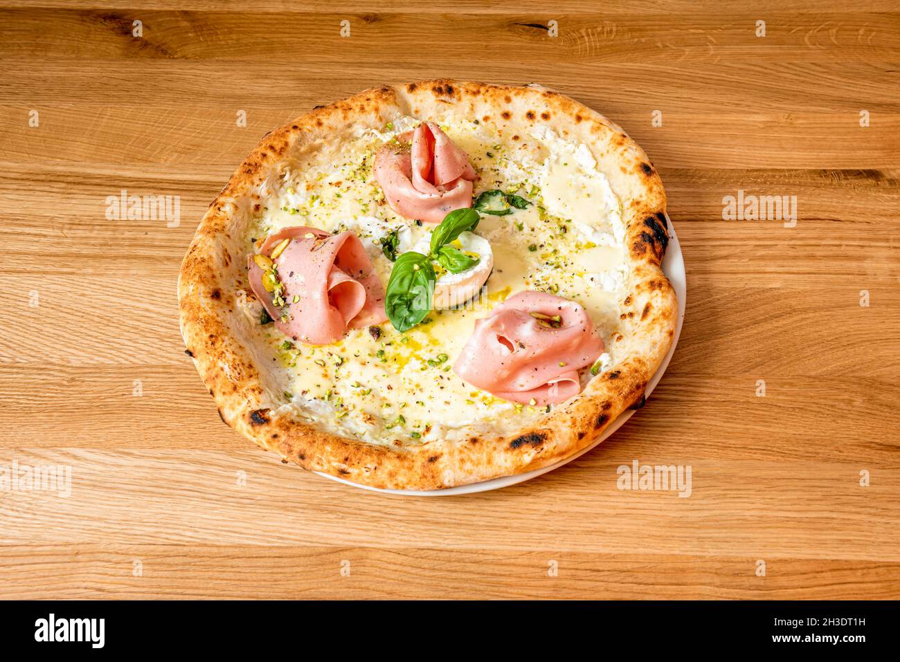 Piccola pizza al forno a crosta sottile con formaggio di capra, mortadella  a fette, foglie di basilico, pistacchi e olio d'oliva con origano Foto  stock - Alamy