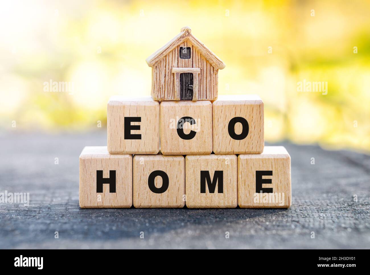 Piccola casa giocattolo in piedi su blocchi di lettere di legno lettura ECO HOME contro uno sfondo sfocato foresta autunno. Concetto di casa a basso impatto ambientale. Foto Stock