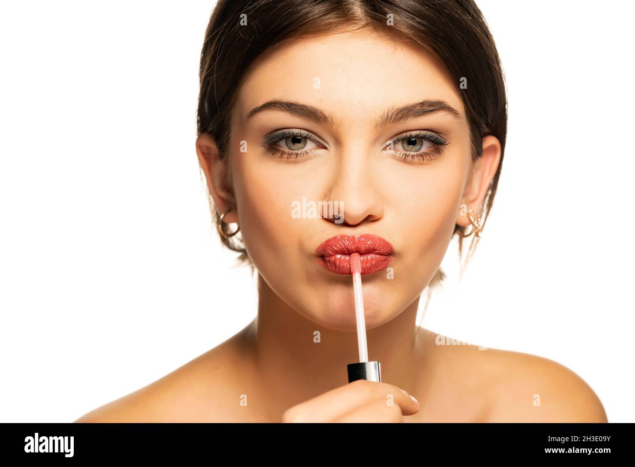una giovane bella donna applica la lucentezza del labbro su uno sfondo bianco Foto Stock