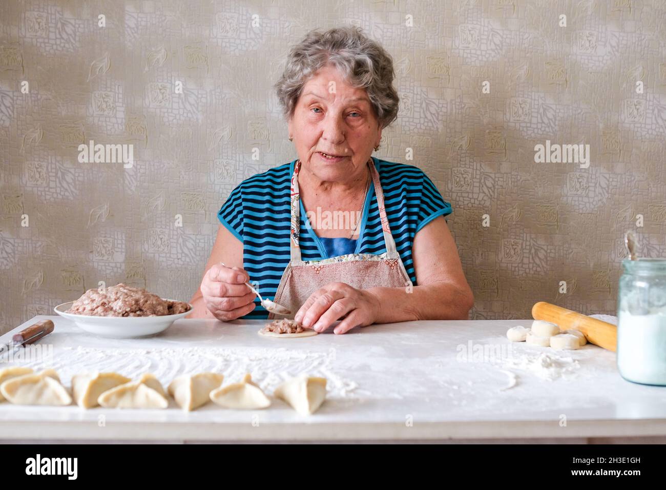 La nonna produce manti, mette la carne tritata su un pezzo di pasta rotonda con un cucchiaio Foto Stock