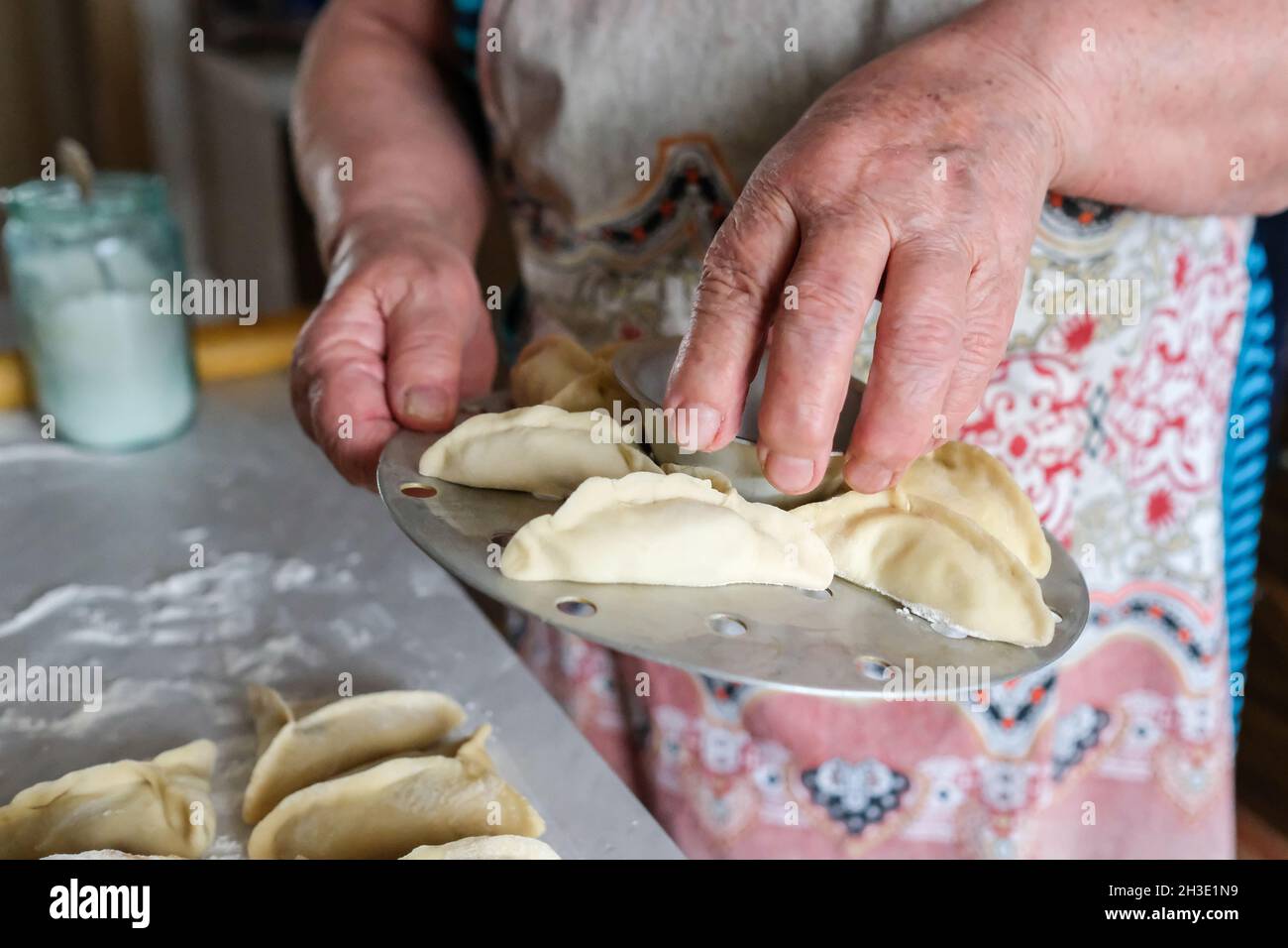 Mantovarka e le mani della nonna. manti crudo su uno speciale dispositivo da cucina Foto Stock