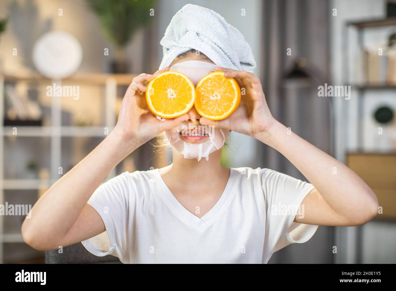 Primo piano ritratto di graziosa femmina teenger con asciugamano sulla  testa e maschera sul viso che copre gli occhi con fette di arance.  Cosmetici minerali e vitaminici per la cura della pelle