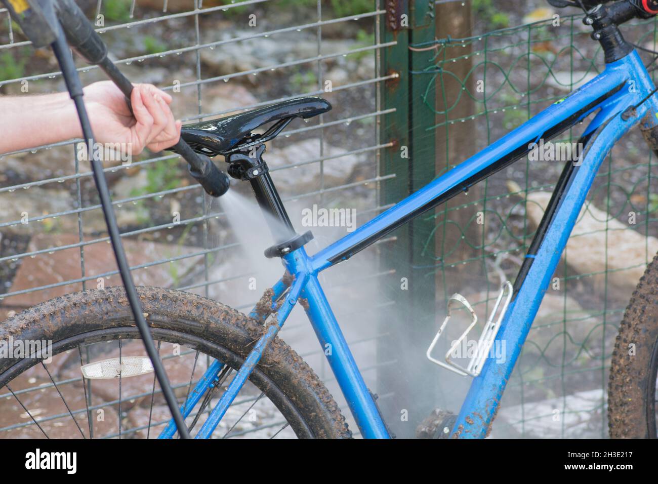 Uomo che pulisce la bicicletta blu usando il lavaggio ad alta pressione Foto Stock