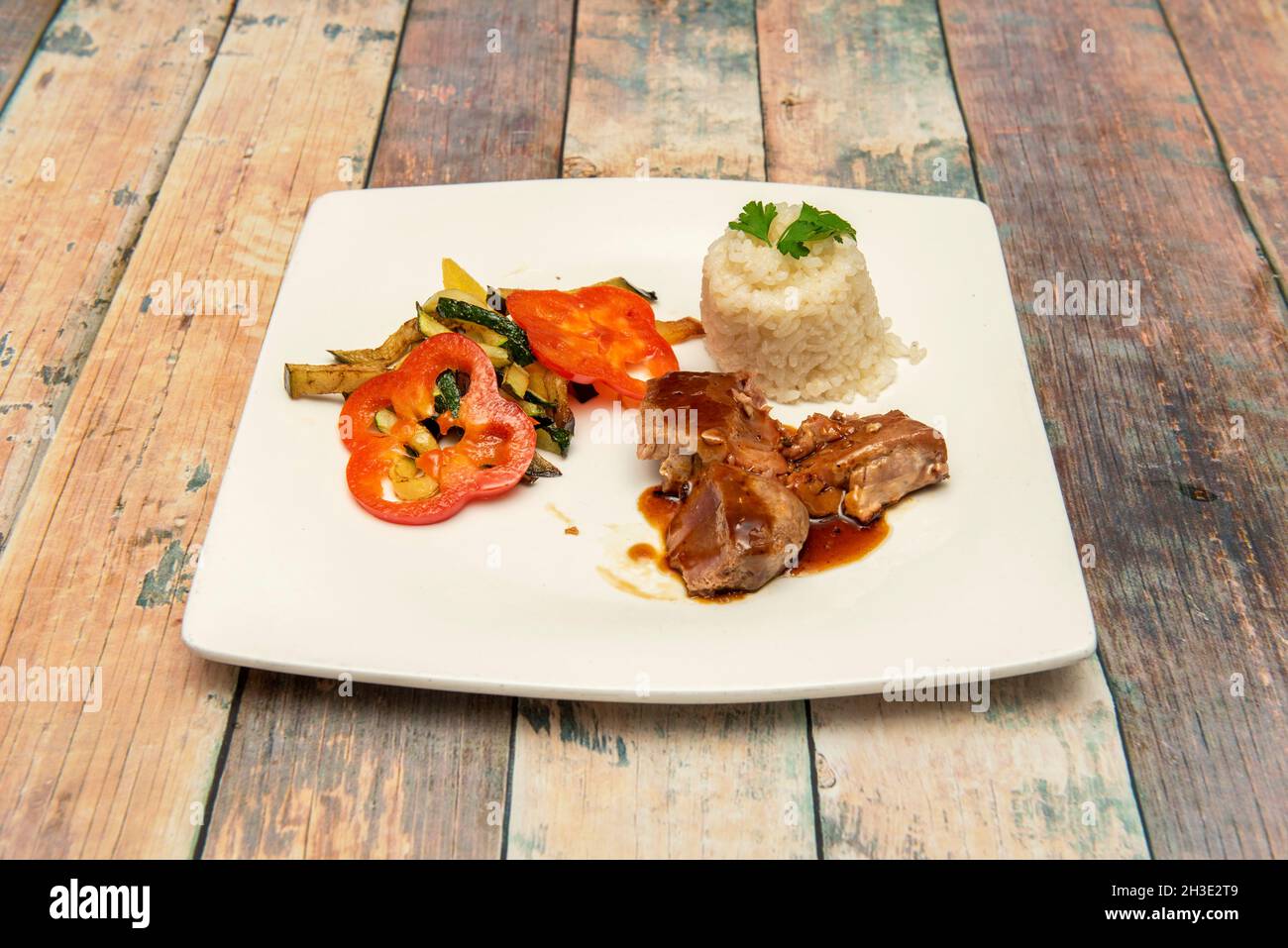 porzione di tonno stufato con guarnitura di verdure stufate e ciotola di riso bianco su tavola di legno Foto Stock