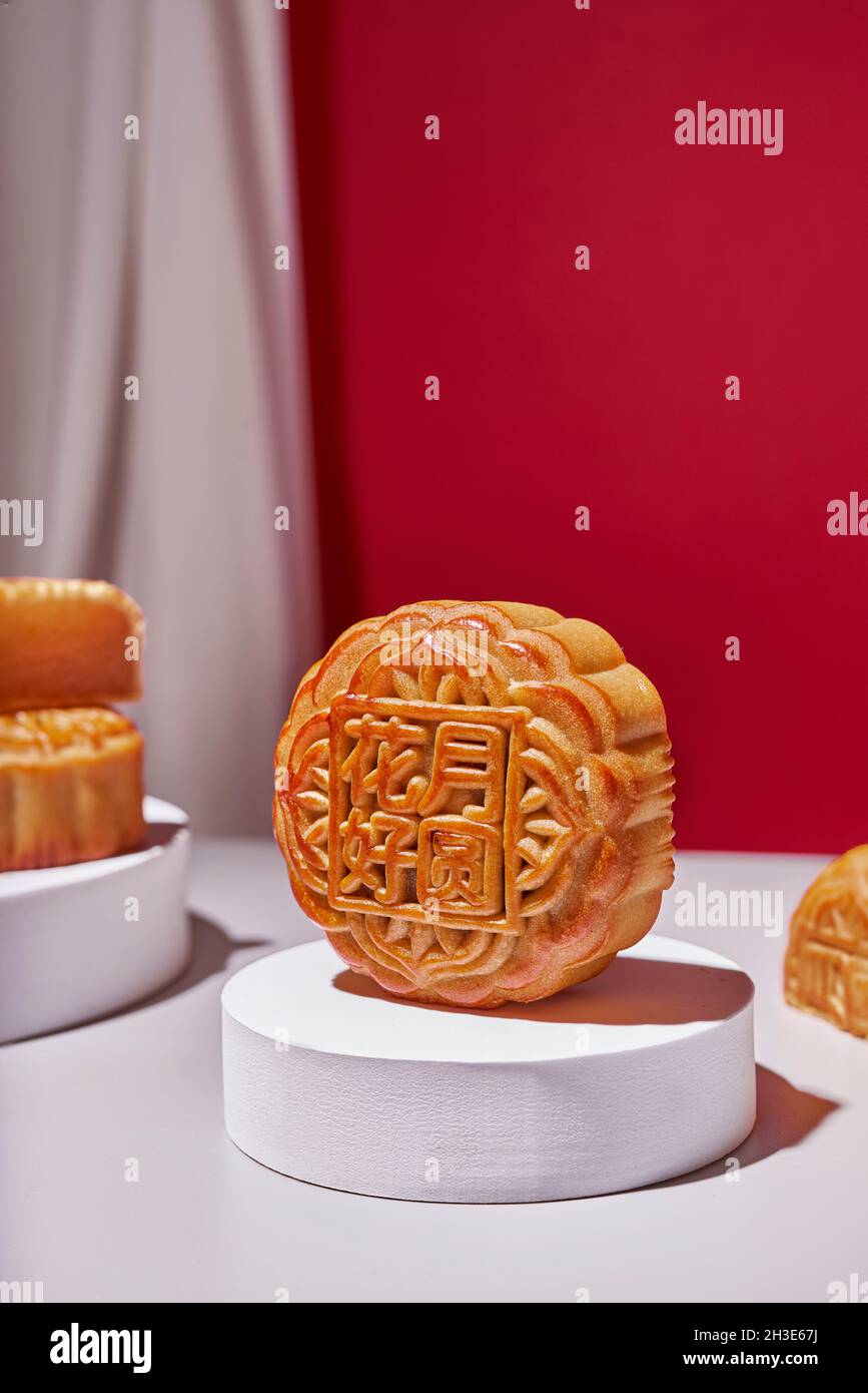 Rotonda tradizionale dolce torta di mooncake cinese servita su un tavolo con fiori su sfondo rosso in moderno studio luminoso Foto Stock