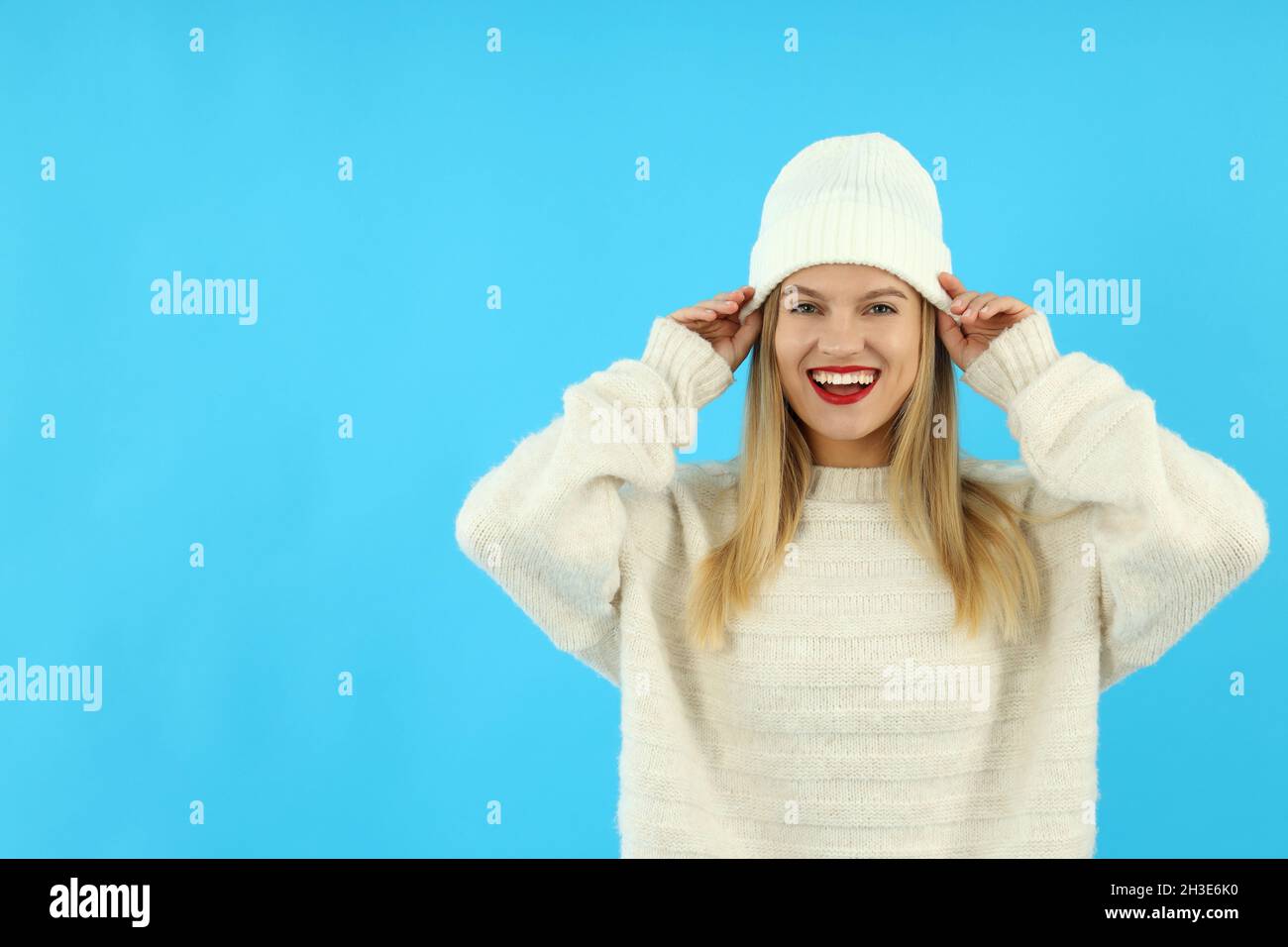 Ragazza attraente in cappello di lana e maglione su sfondo blu. Foto Stock