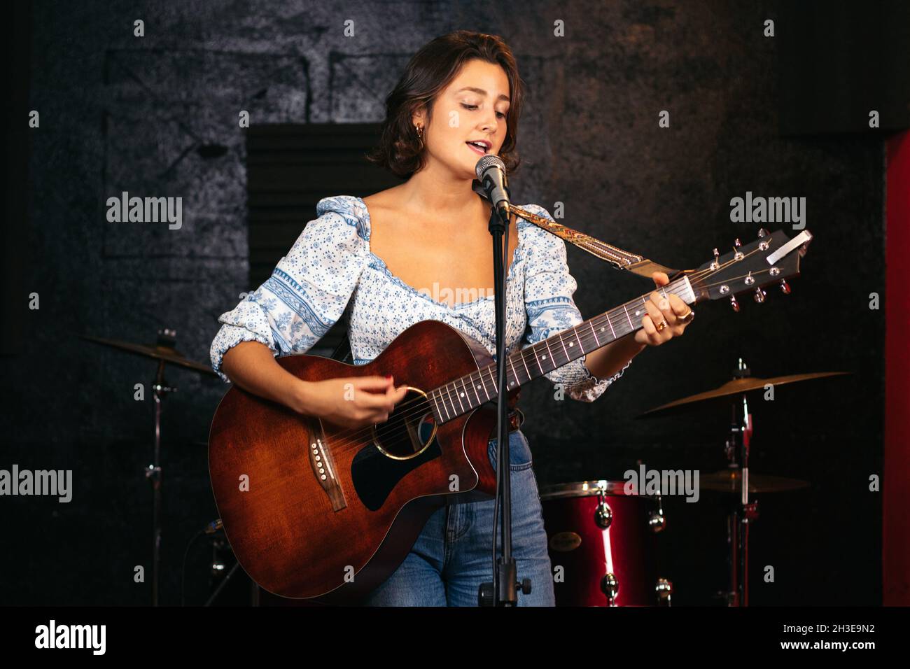 Fidata signora con chitarra cantare nel microfono mentre si esibisce la canzone in un club luminoso Foto Stock