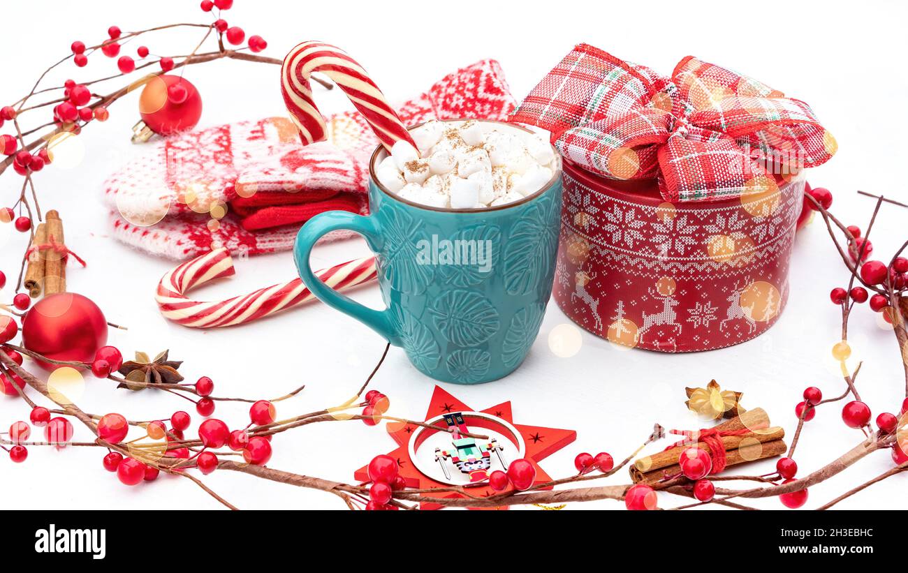 Natale dando tempo. Primo piano della confezione regalo rotonda rossa circondata da decorazioni natalizie in tonalità bianche e rosse. Un regalo di Natale e una tazza di cioccolata calda Foto Stock