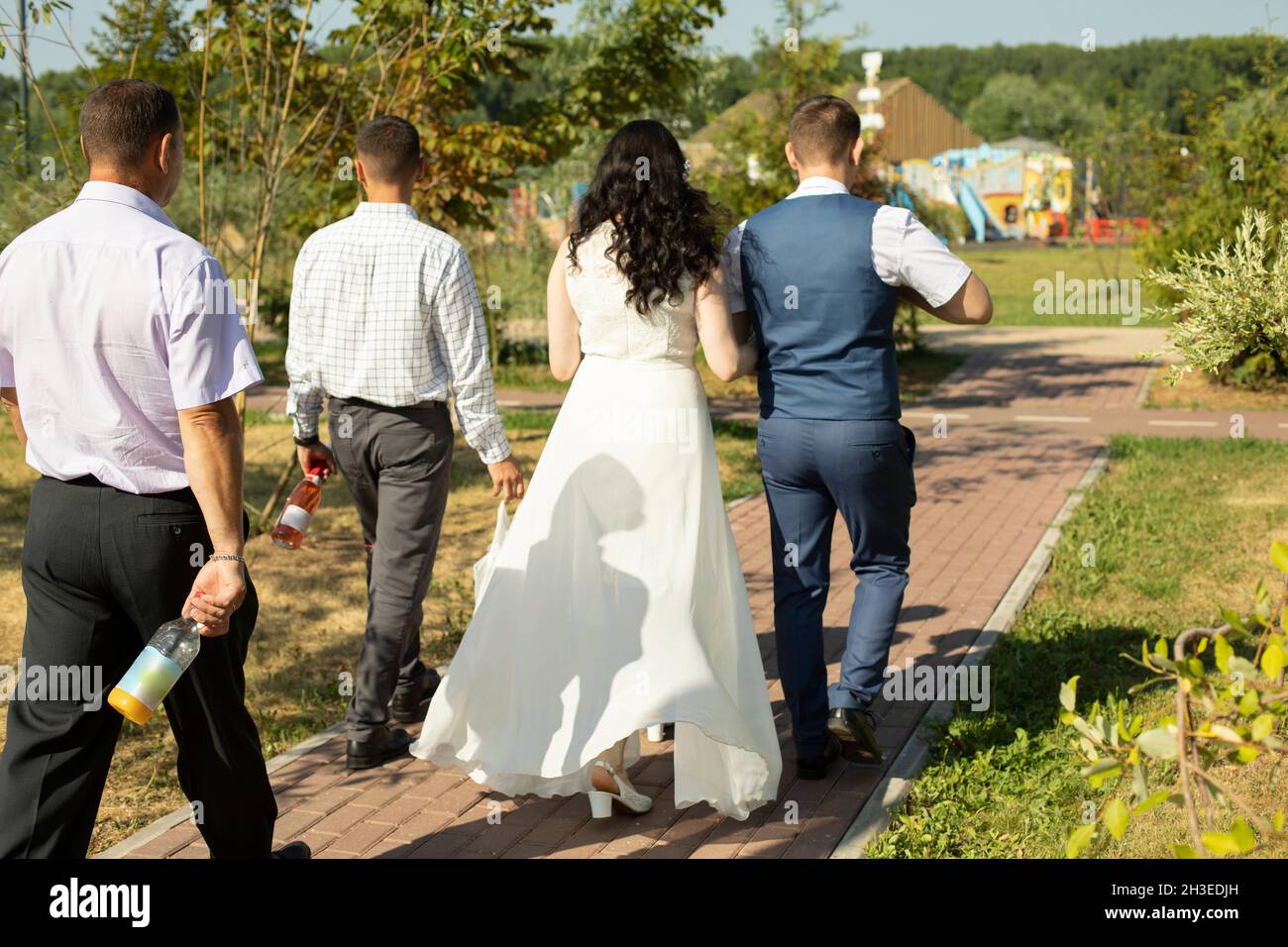 La gente cammina lungo la strada durante un matrimonio. Quattro persone in  abiti eleganti, uomini in camicie e pantaloni, la sposa in un abito bianco.  Celebrazione in t Foto stock - Alamy