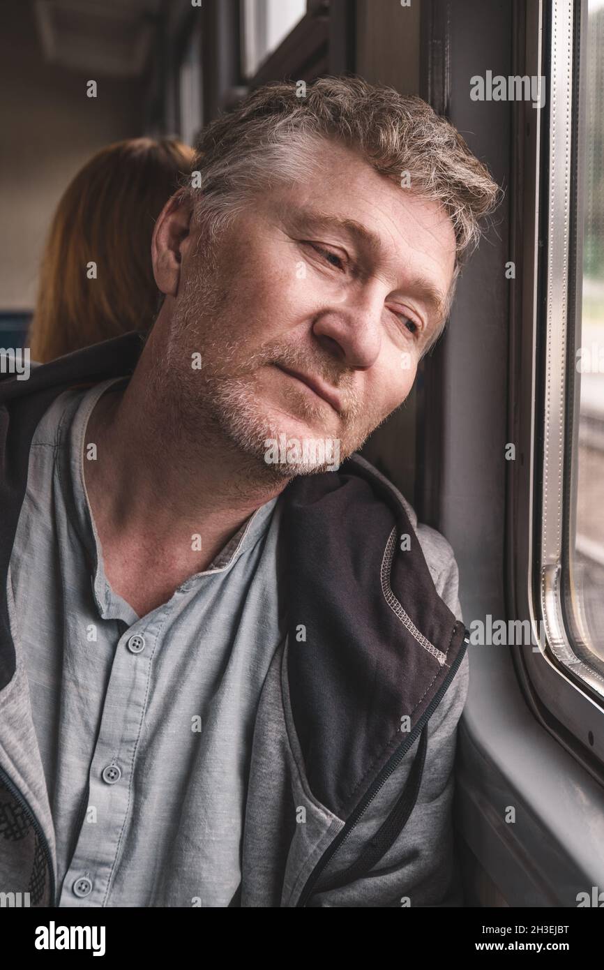 L'uomo di mezza età, bello e premuroso, siede nel carrello di un vecchio treno elettrico e guarda fuori dalla finestra. Lavorare in un'altra città. Viaggi tra città Foto Stock
