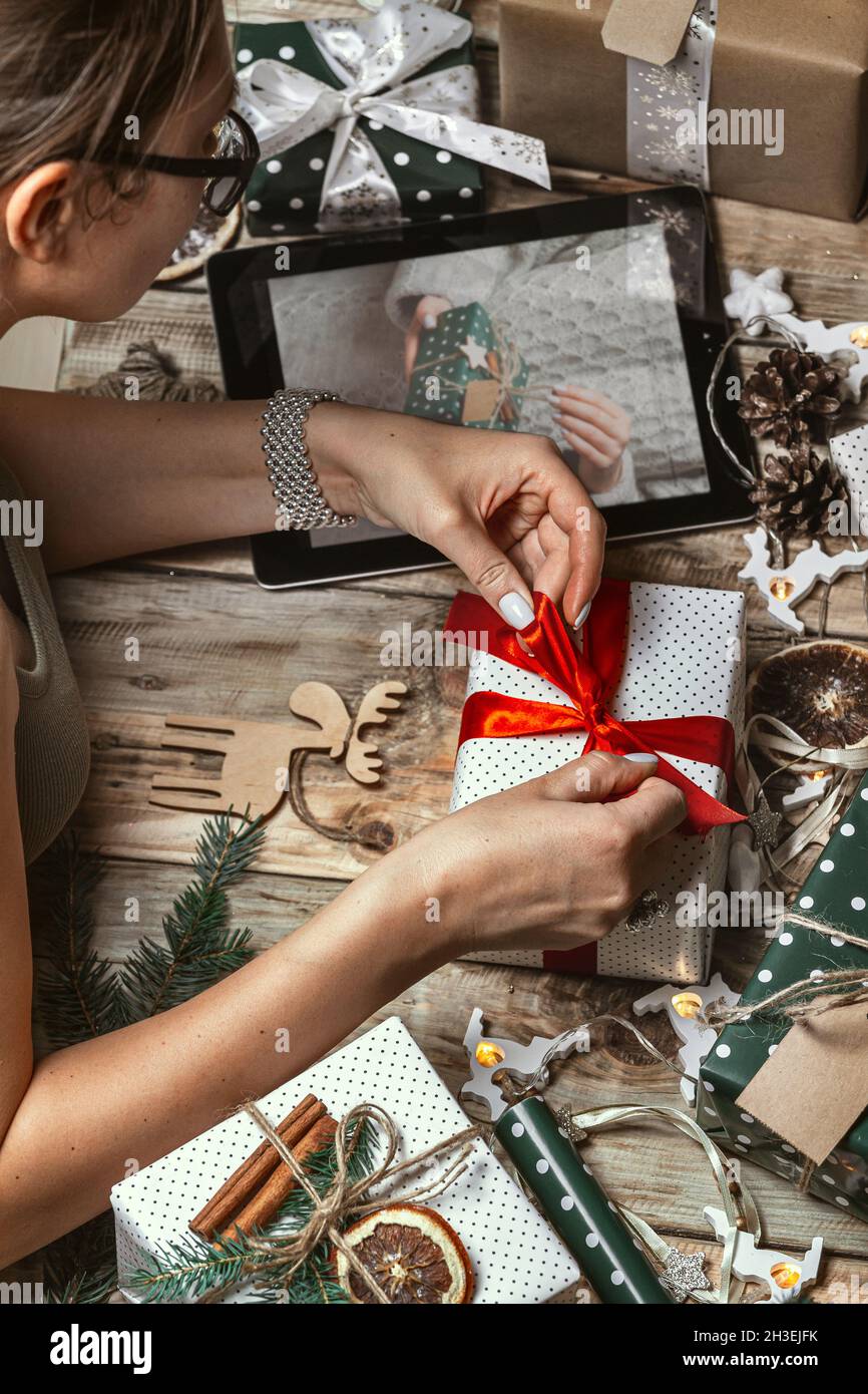 Donna mani avvolgere regalo di natale con tablet sul tavolo con chr Foto Stock